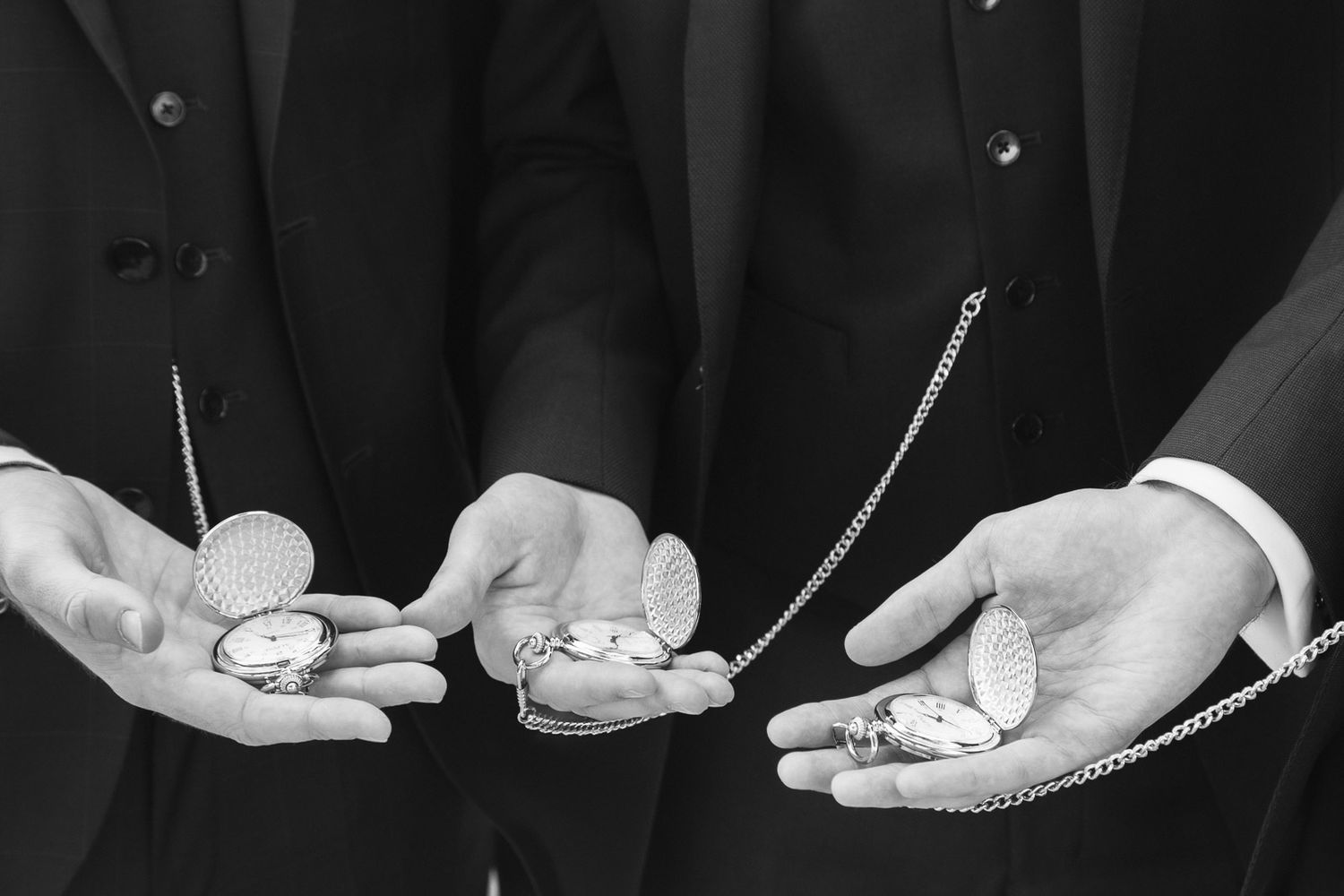 Three men in suits displaying pocket watches with chains in their open palms, black and white photo.