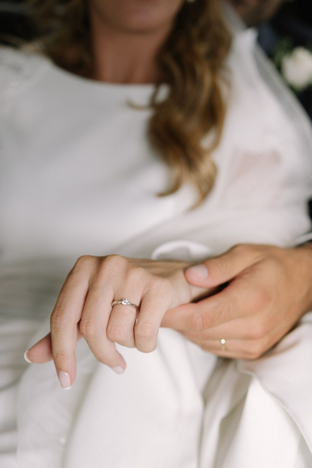 Close-up of a bride in white dress displaying her diamond engagement ring on her finger at a wedding.