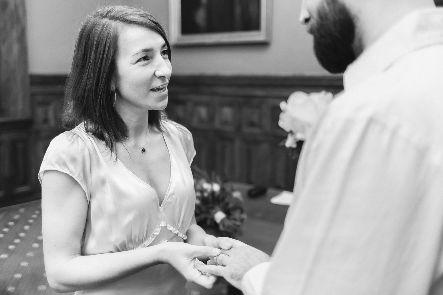 Black and white photo of a woman smiling and holding hands with a man during a wedding ceremony.