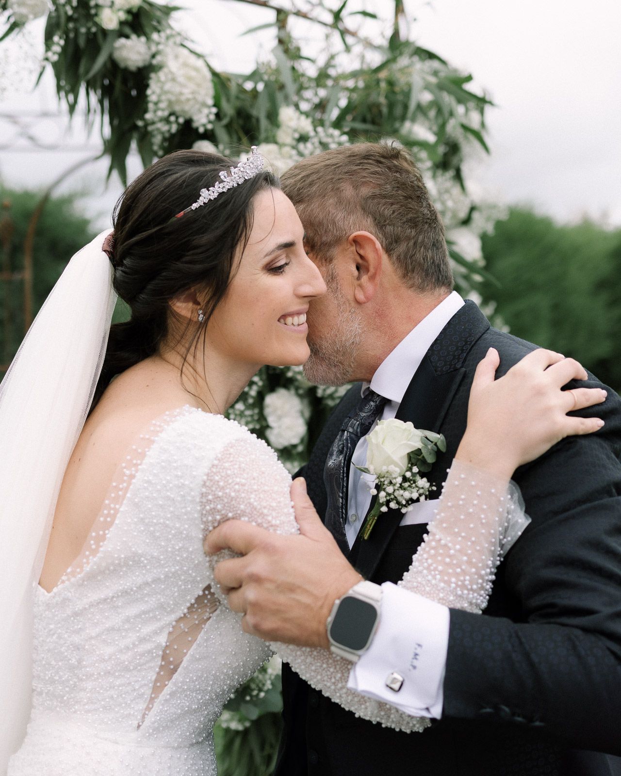 A bride and groom share a romantic kiss at their wedding ceremony, surrounded by white floral arrangements.