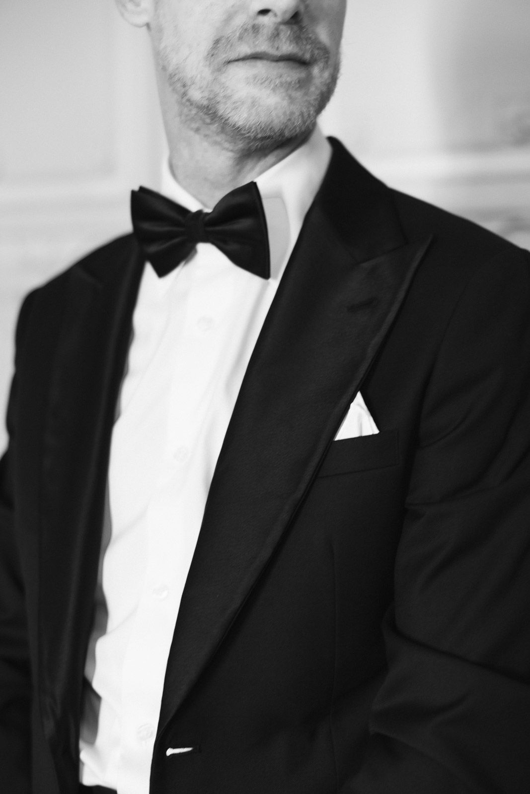 Man in black tuxedo with bow tie and white pocket square, elegant formal attire in black and white photo.