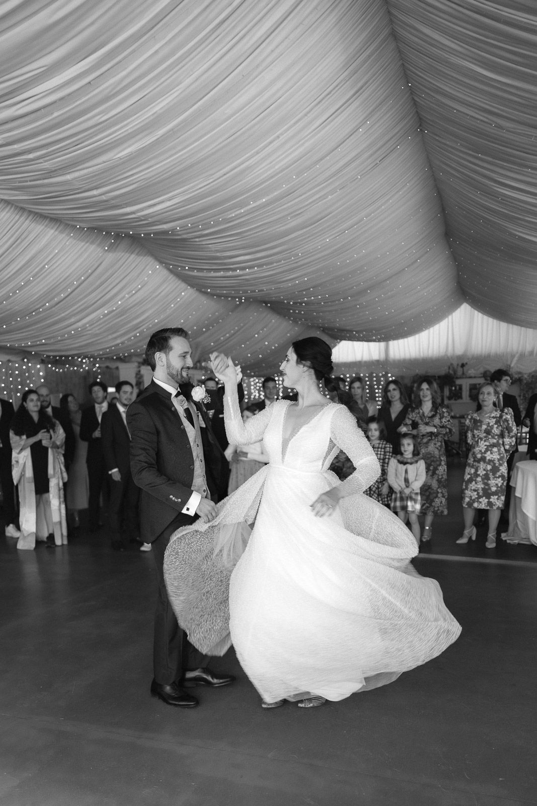 Black and white photo of bride and groom sharing their first dance under draped ceiling at elegant wedding reception.