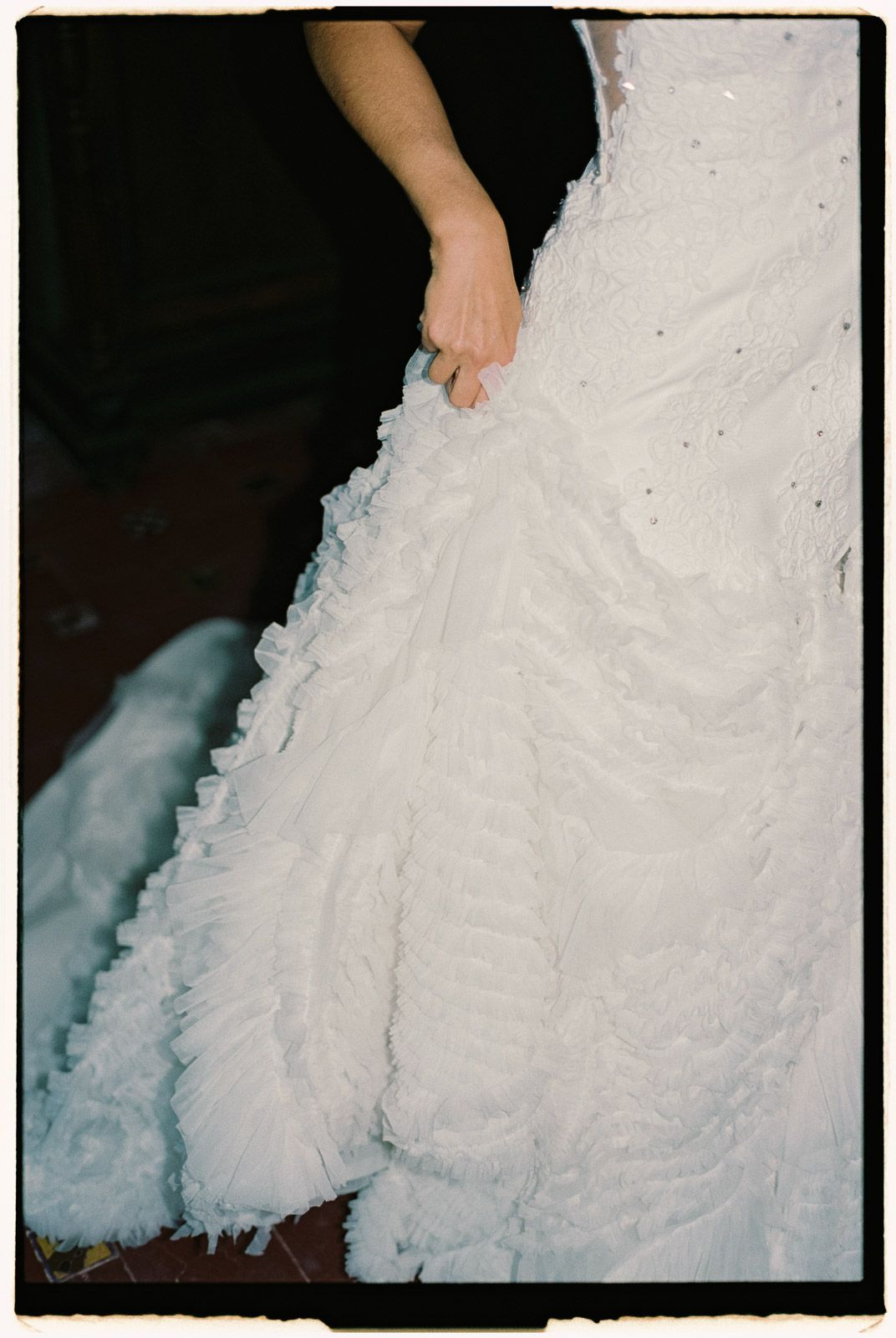 Close-up of a bride holding her ruffled white wedding gown with a diamond ring on her finger.