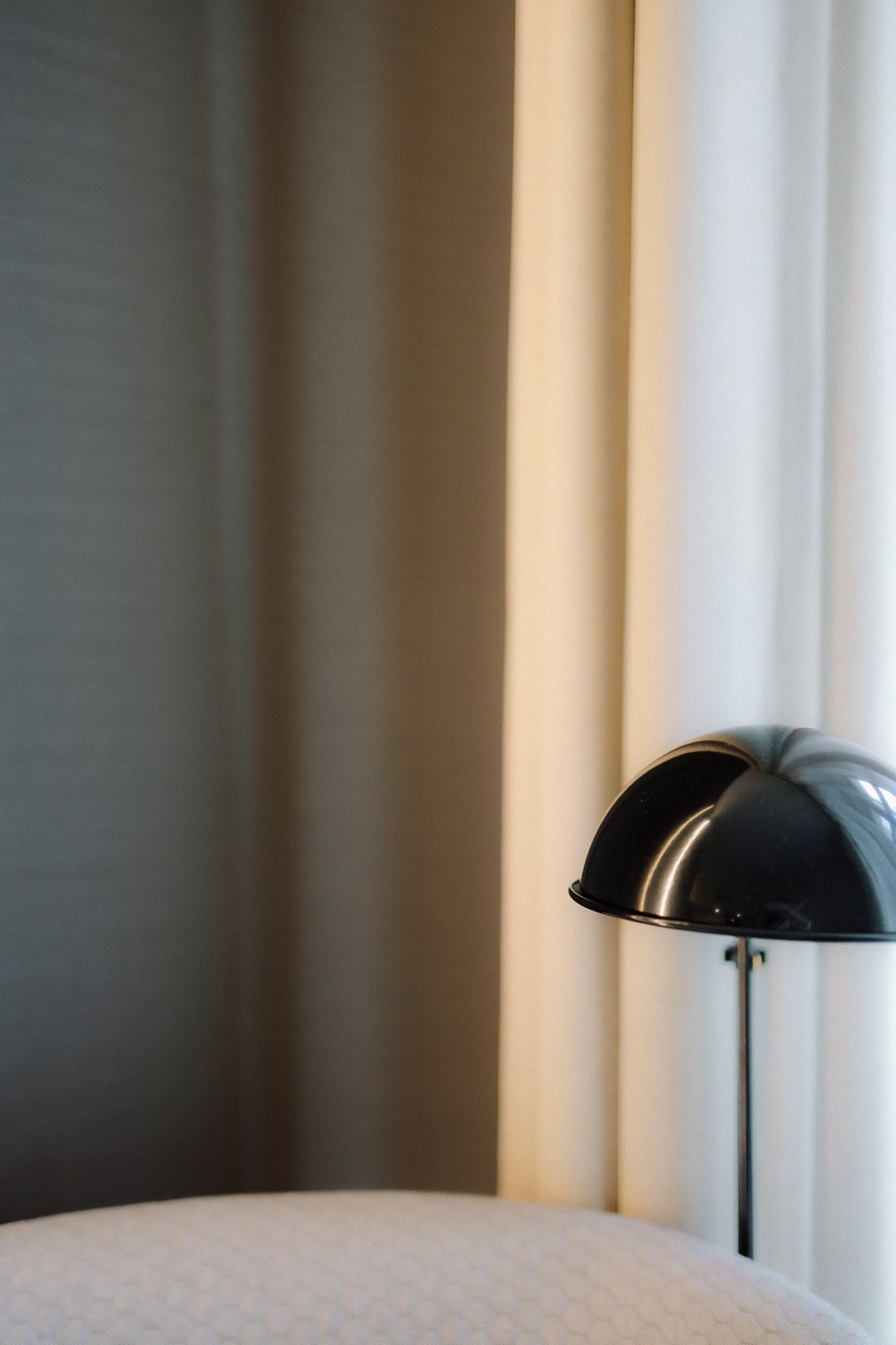Modern black dome table lamp on a bedside table beside elegant cream curtains in a contemporary bedroom.