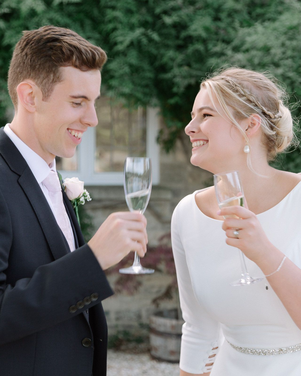 Bride and groom smiling and toasting with champagne flutes at their outdoor wedding celebration.