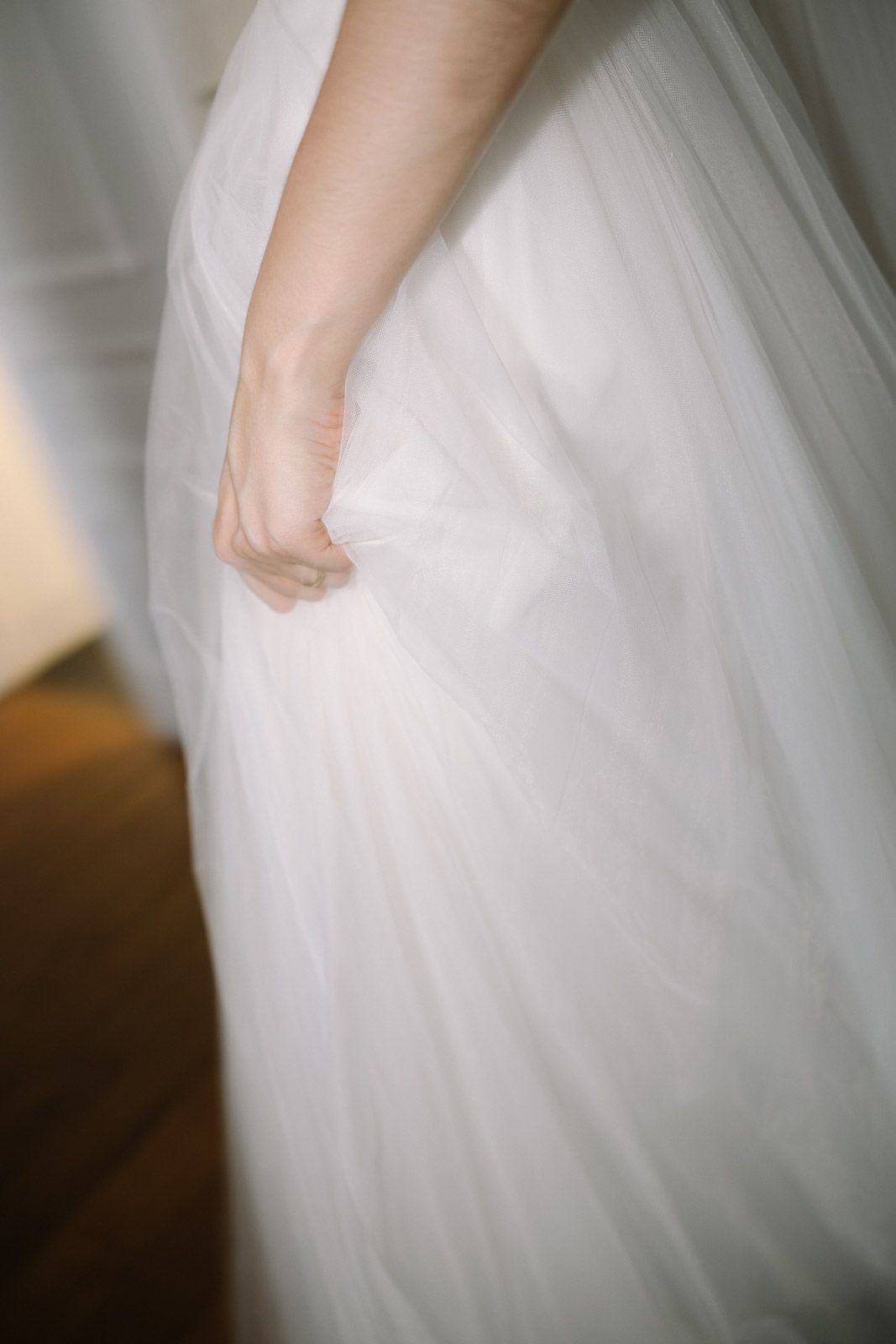 Close-up of a bride holding her flowing white tulle wedding gown skirt with delicate hand.