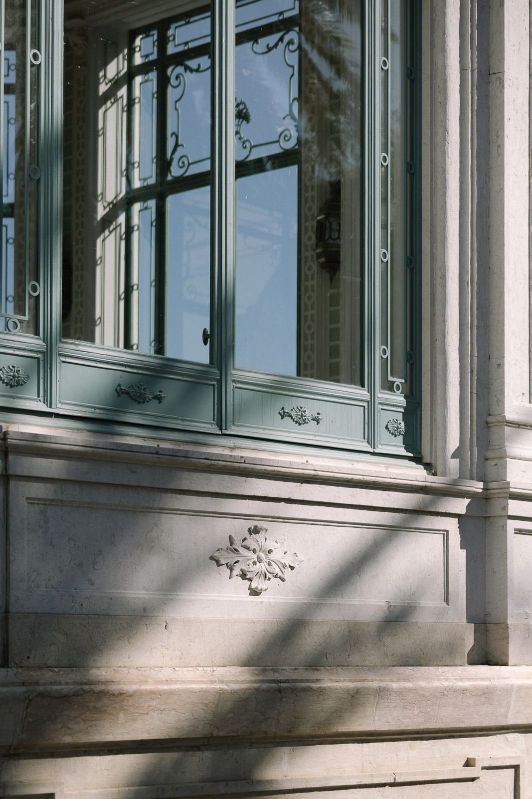 Elegant French architecture featuring ornate green-painted windows with iron details on stone facade.