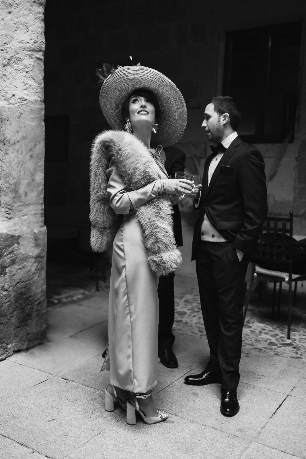Elegant black and white photo of a woman in a wide-brim hat and fur stole with a tuxedo-clad man.