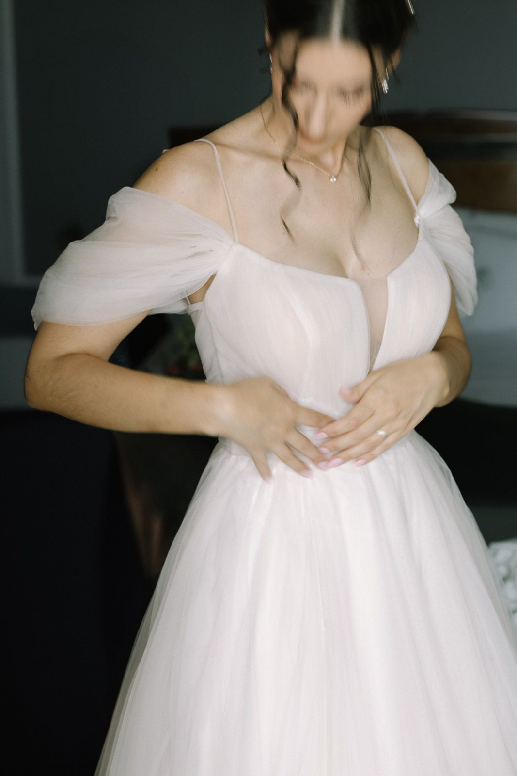 Bride in elegant white off-shoulder tulle wedding gown being helped into dress, soft romantic photography.