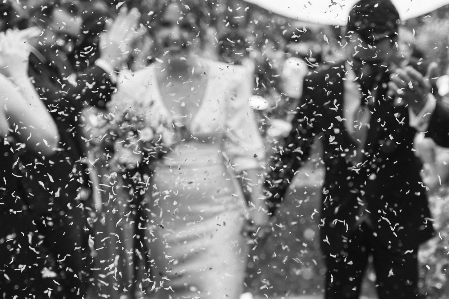 Black and white photo of a couple walking through confetti shower at their wedding celebration.
