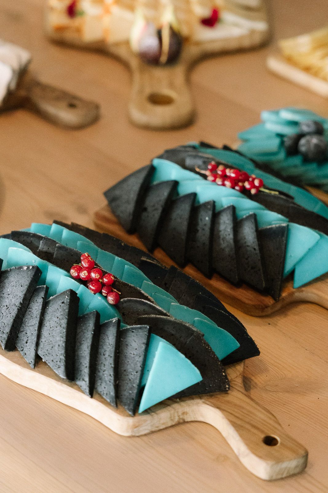 Artistic black and teal triangular cheese slices garnished with red pomegranate seeds arranged on wooden serving boards.