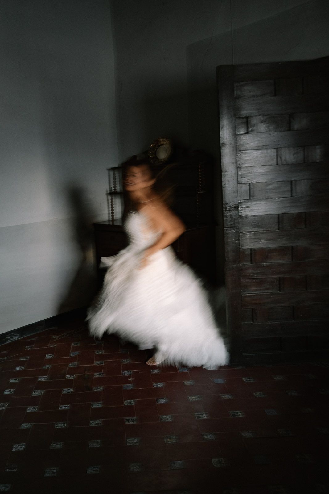 Blurred motion photo of a bride in a white wedding dress spinning indoors near a rustic wooden door.