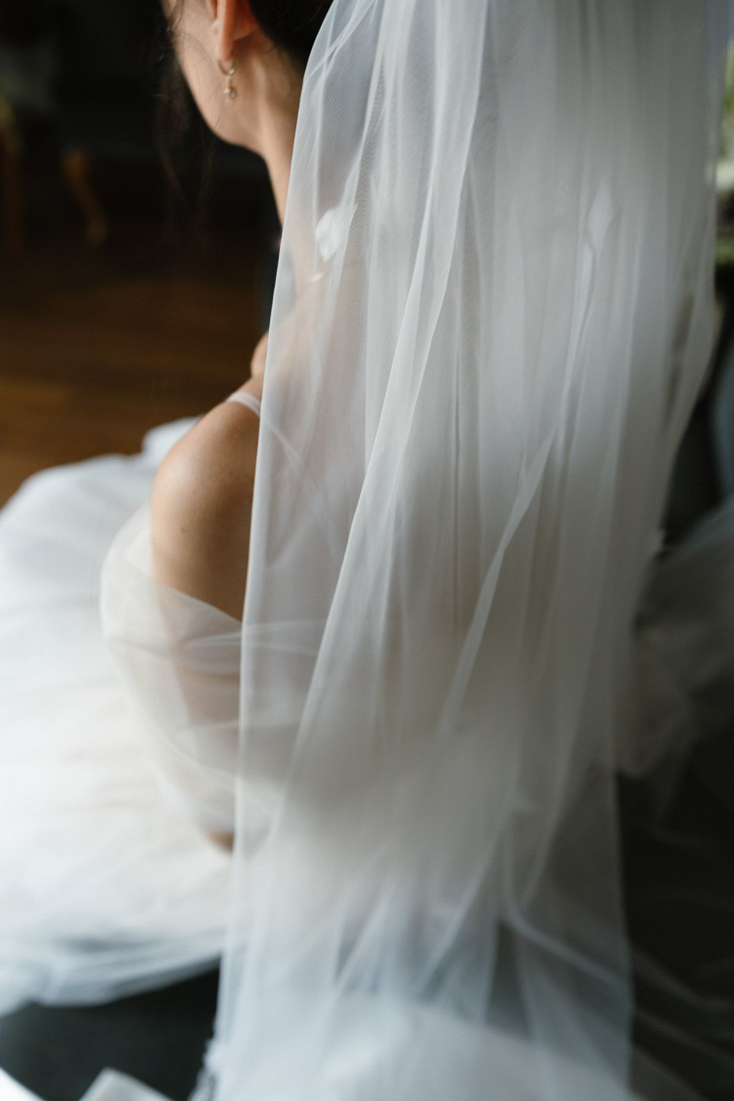 Bride in a white wedding dress and flowing veil, captured from behind in soft natural light.