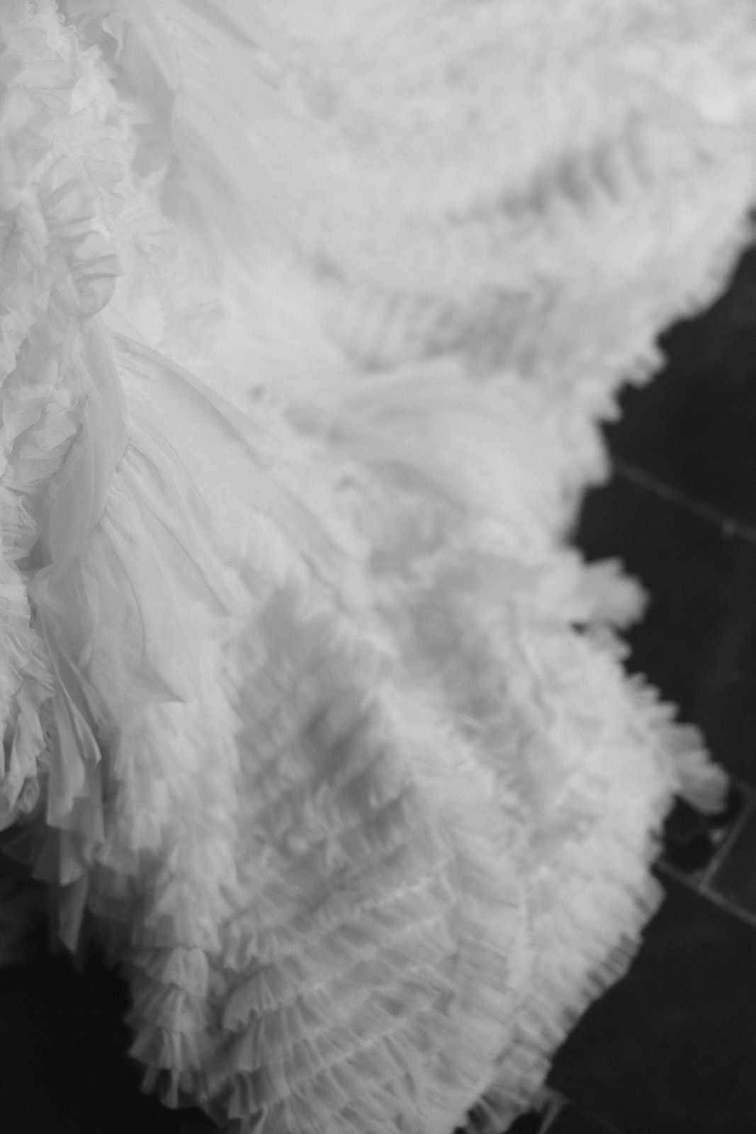 Close-up of a white wedding dress with layered ruffled tulle fabric in black and white photography.
