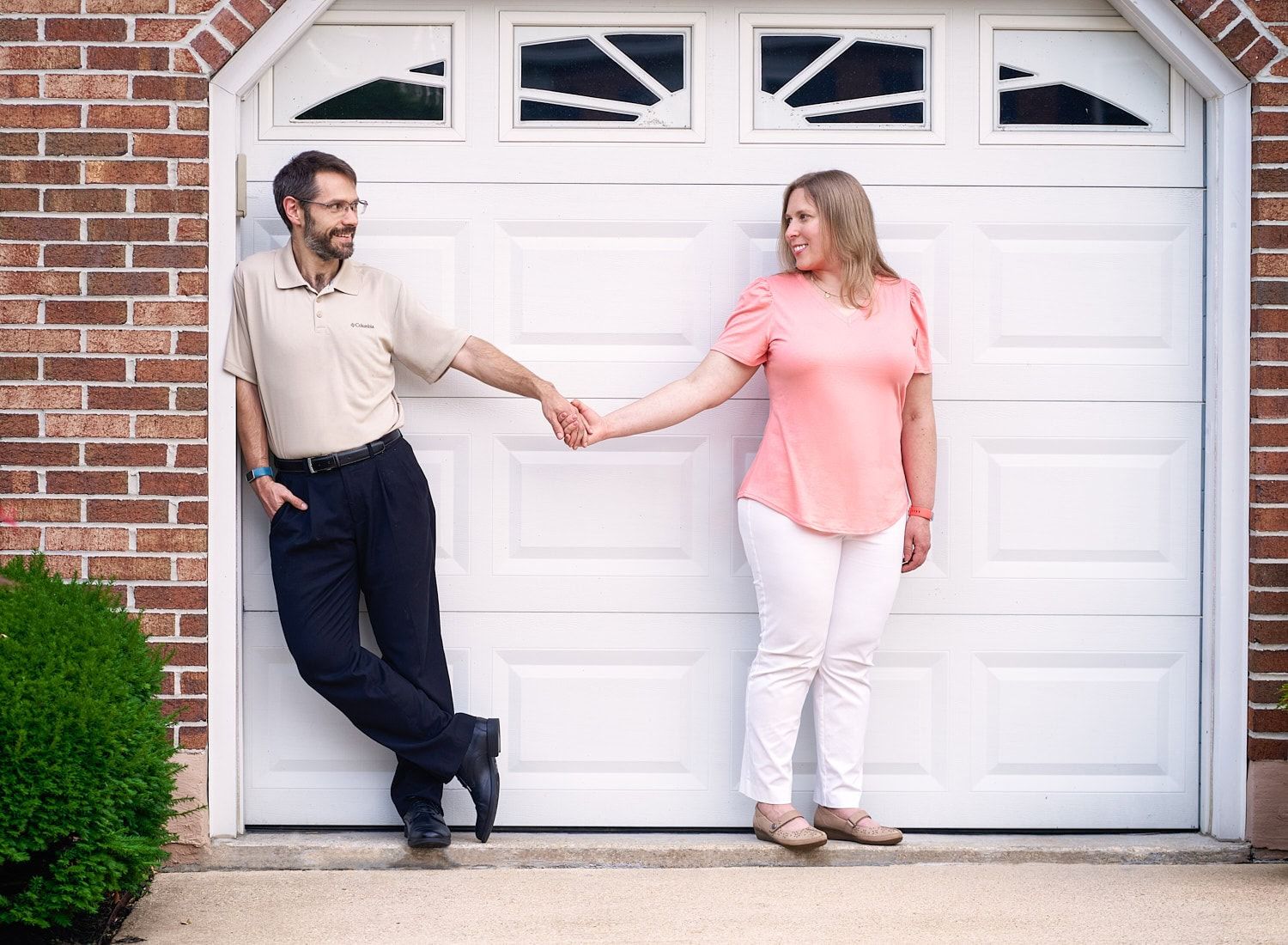Smiling couple holding hands in front of a white garage door, standing apart but connected, during an outdoor Perry Hall family photo sessio