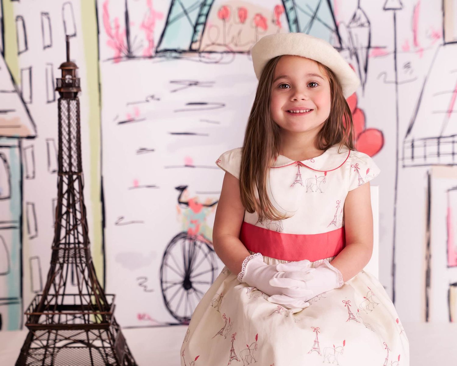 Five-year-old girl with long brown hair wearing an off-white beret and Paris dress sitting in a Parisian photo scene