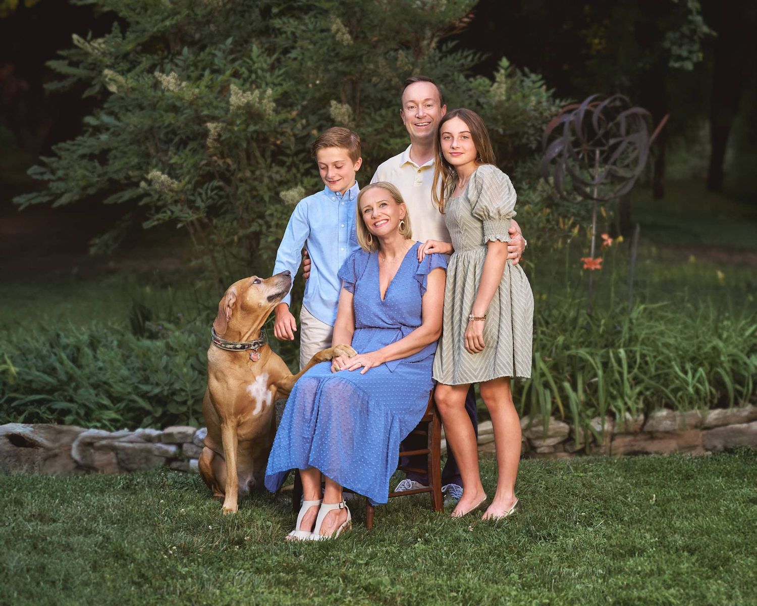 Parents and boy and girl tween with family dog sitting  in front of circular planting