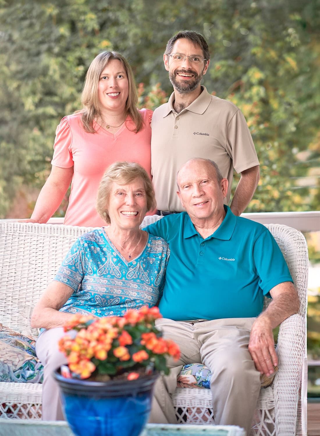 Older parents seated on wicker settee with 30-something daughter and son-in-law standing behind them on their Baltimore County front porch
