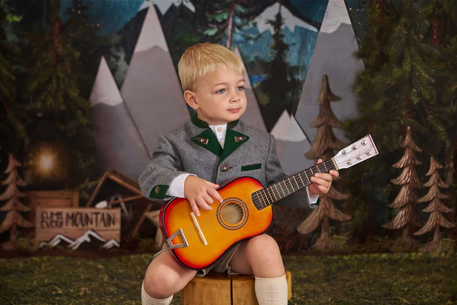 Toddler boy dressed in authentic Austrian garb holding a guitar in a Sound of Music scene