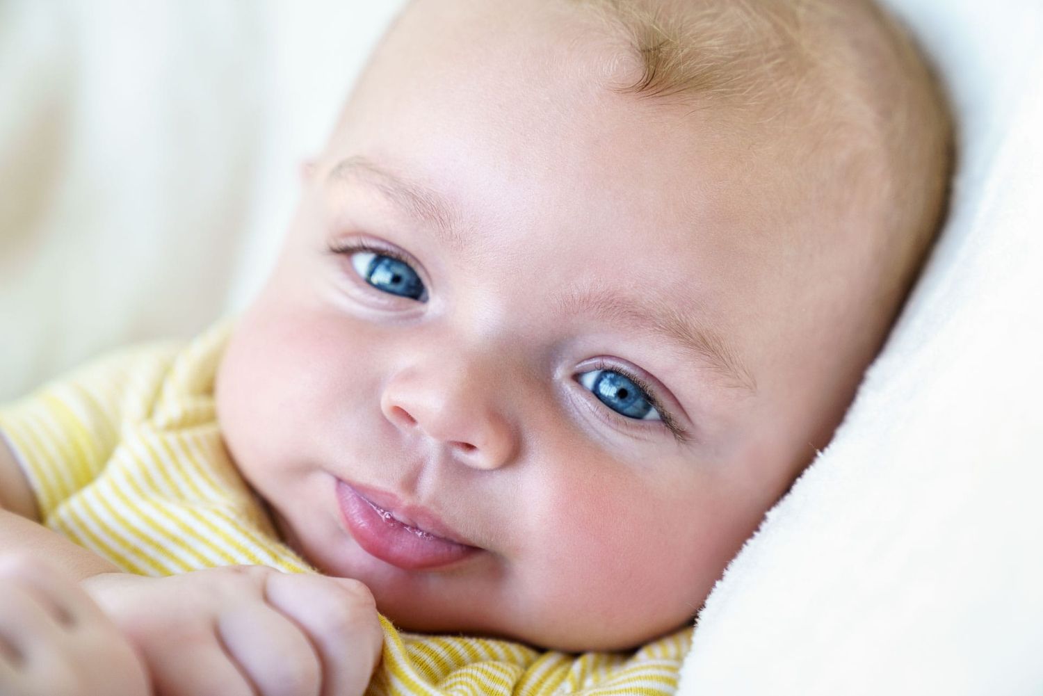 Infant boy in yellow striped shirt blowing baby bubbles