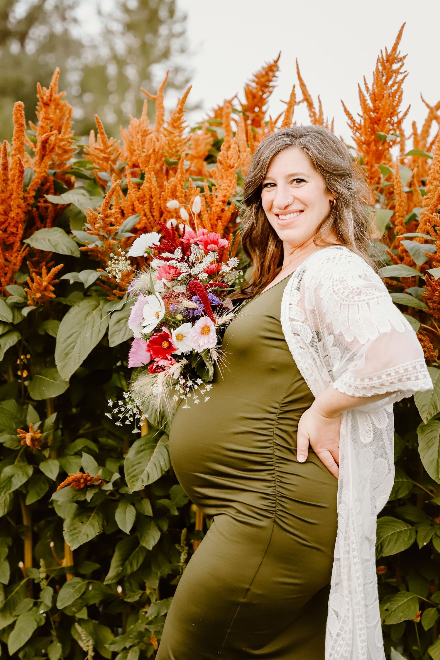 Maternity portrait with colorful bouquet against vibrant orange flowering plants.