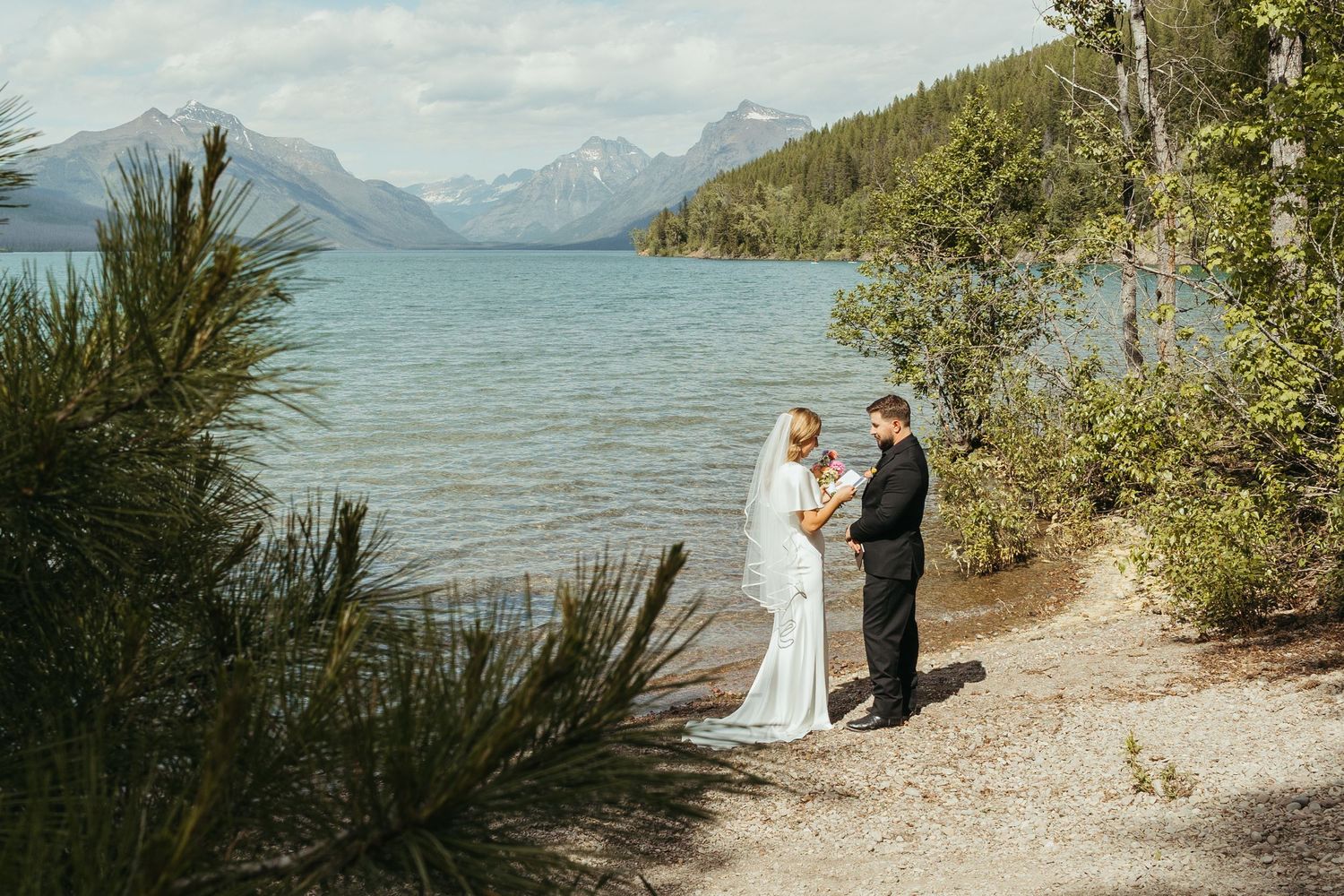 A couple exchanges vows during an intimate lakeside ceremony with mountain views and natural foliage along the shoreline.