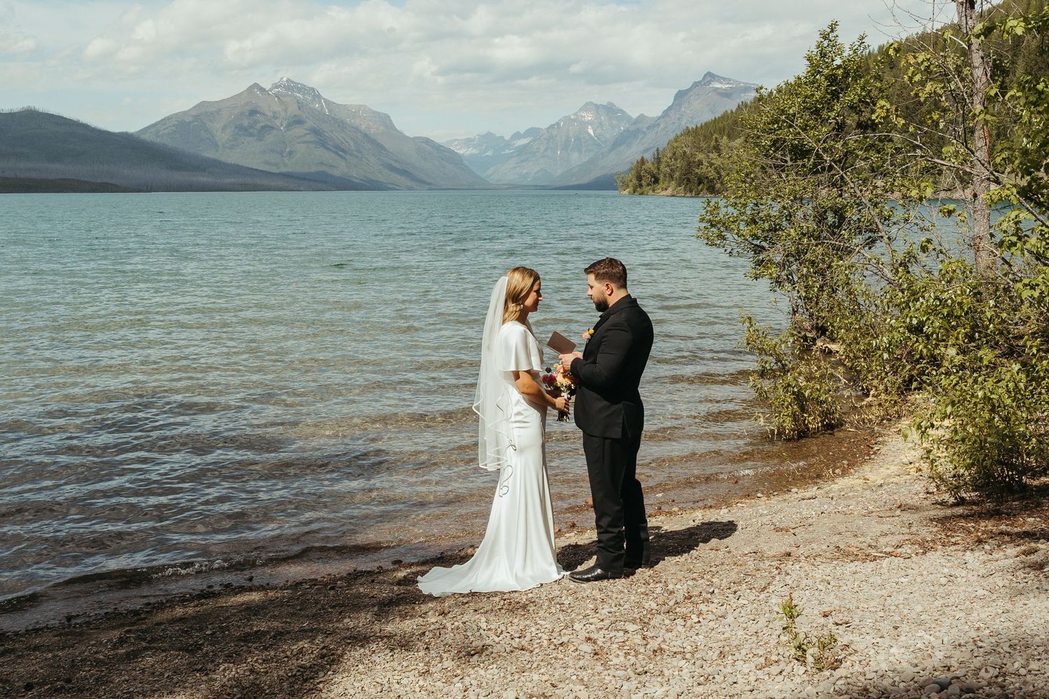 Couple exchanging vows at lakeside wedding ceremony with stunning mountain backdrop at Glacier National Park.