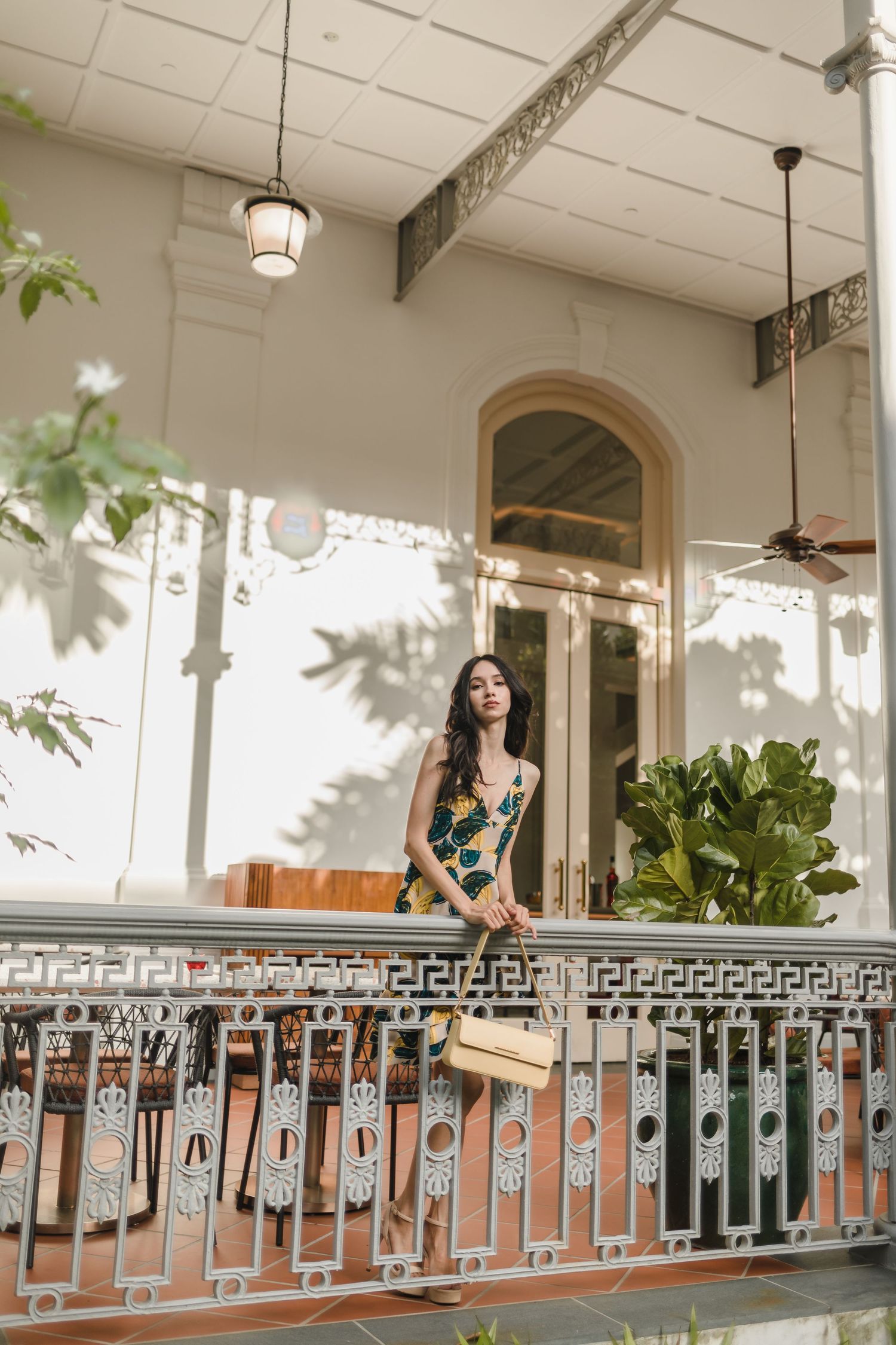 Woman in floral dress poses on ornate vintage balcony with decorative railings.