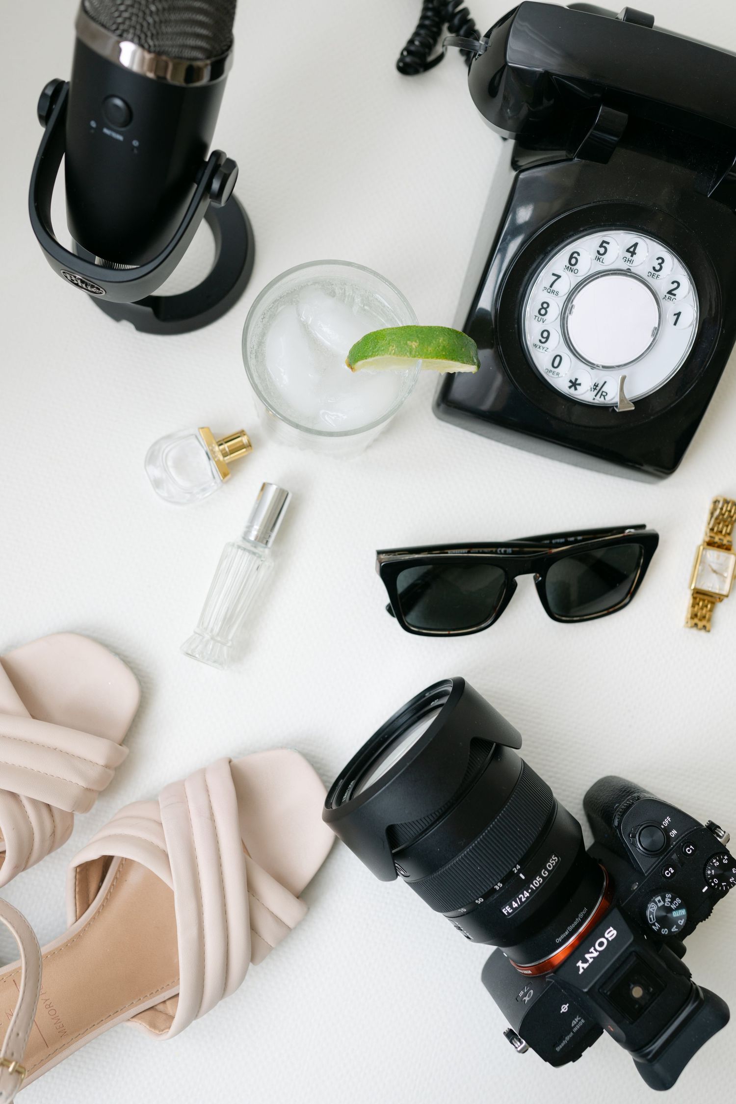 Flatlay photography setup with black camera equipment, lenses, and light-colored fabric on white background.