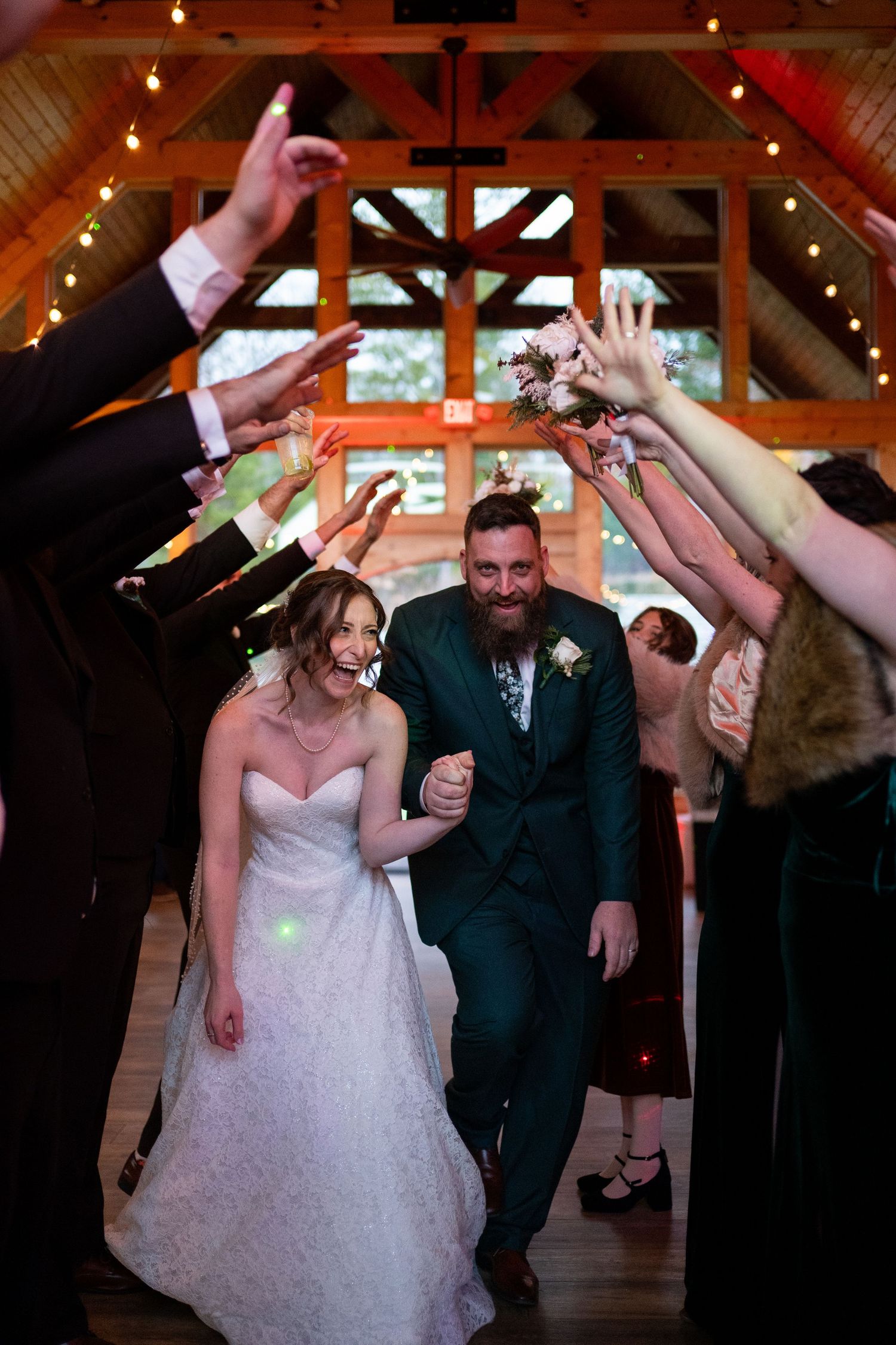 A joyful couple dances together at their rustic barn wedding reception with string lights overhead.