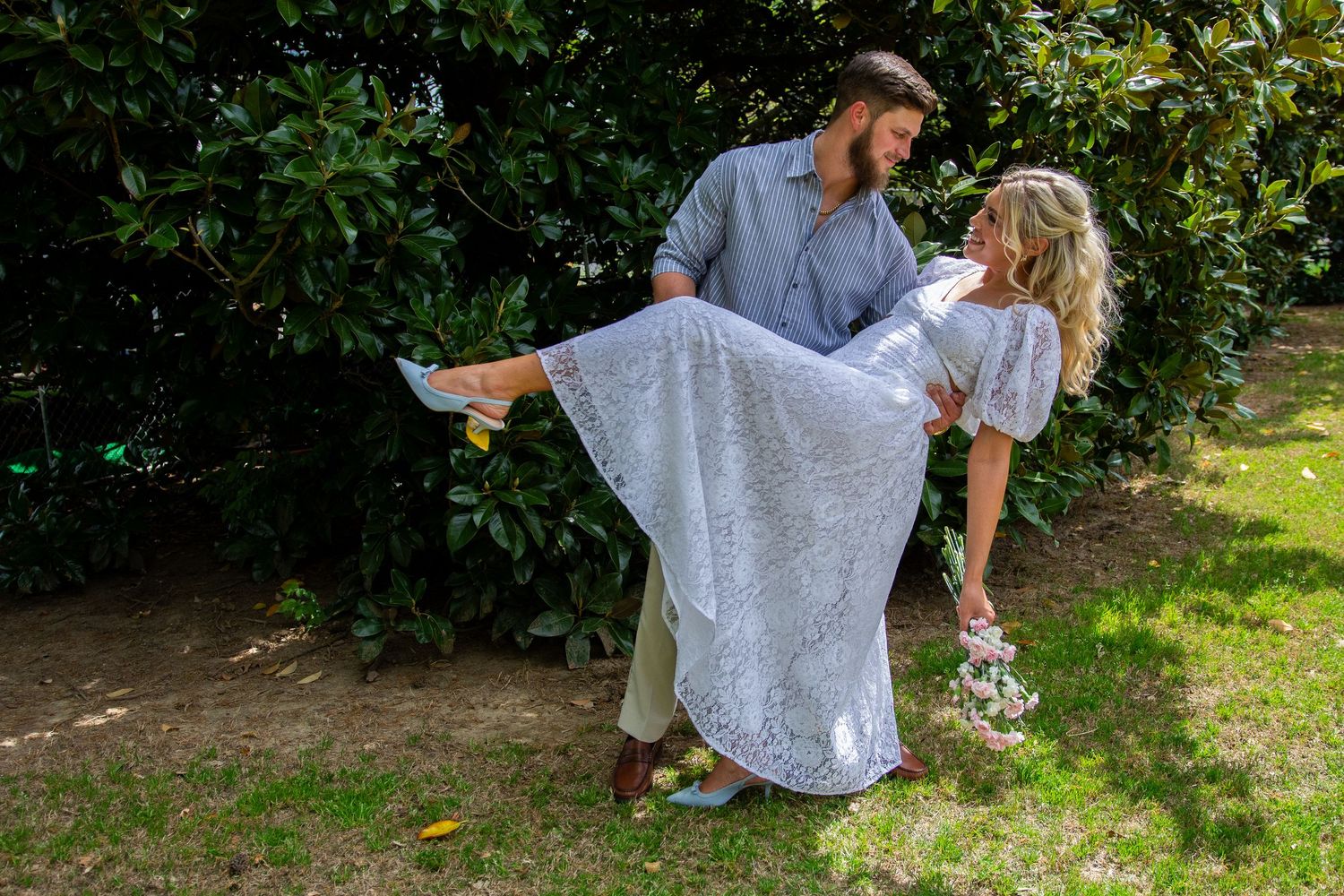 A couple in wedding attire dances together in a garden setting, the bride's white lace dress flowing with movement.
