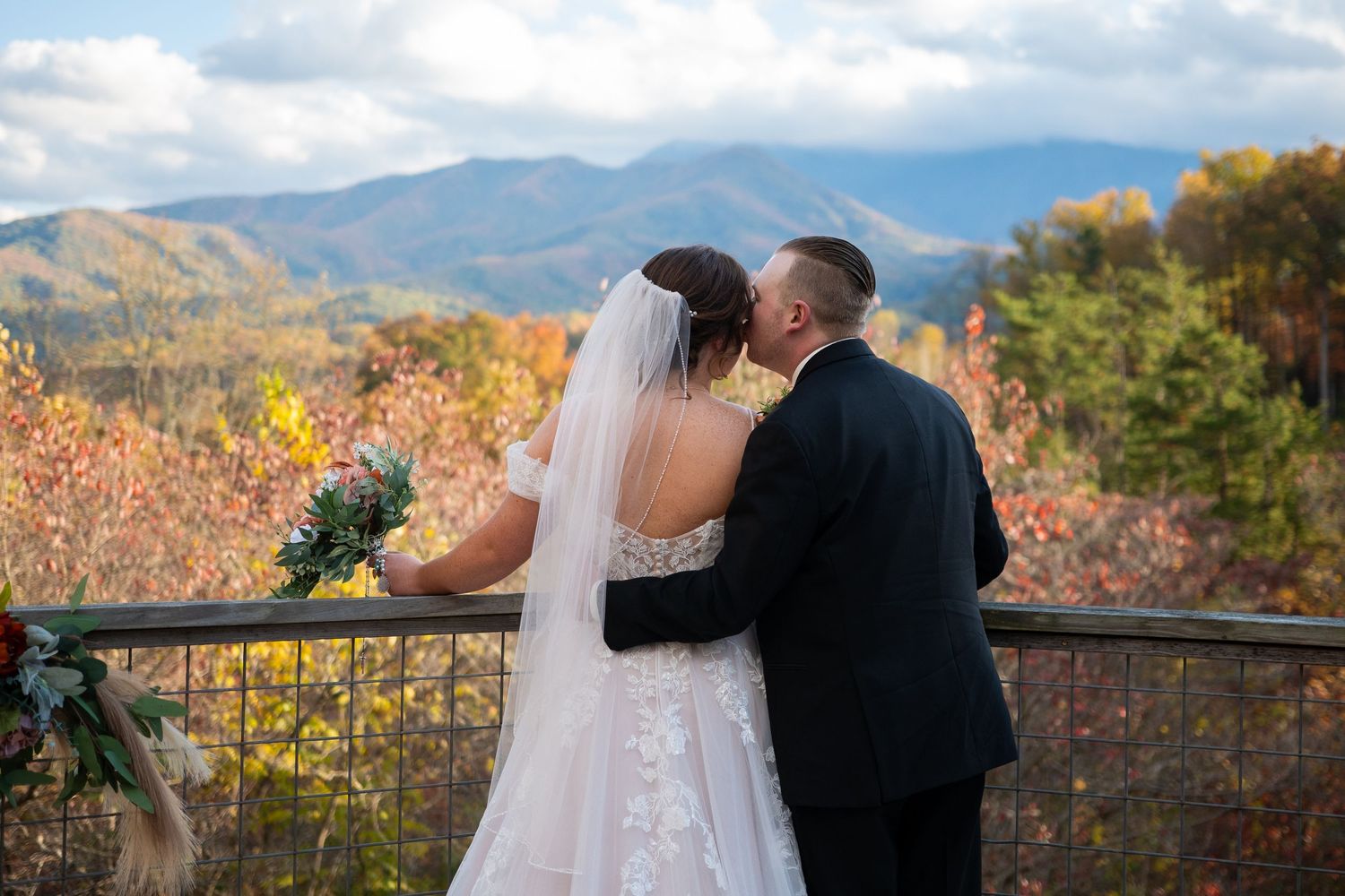 A couple shares a romantic moment on a scenic mountain overlook during autumn with colorful fall foliage in view.