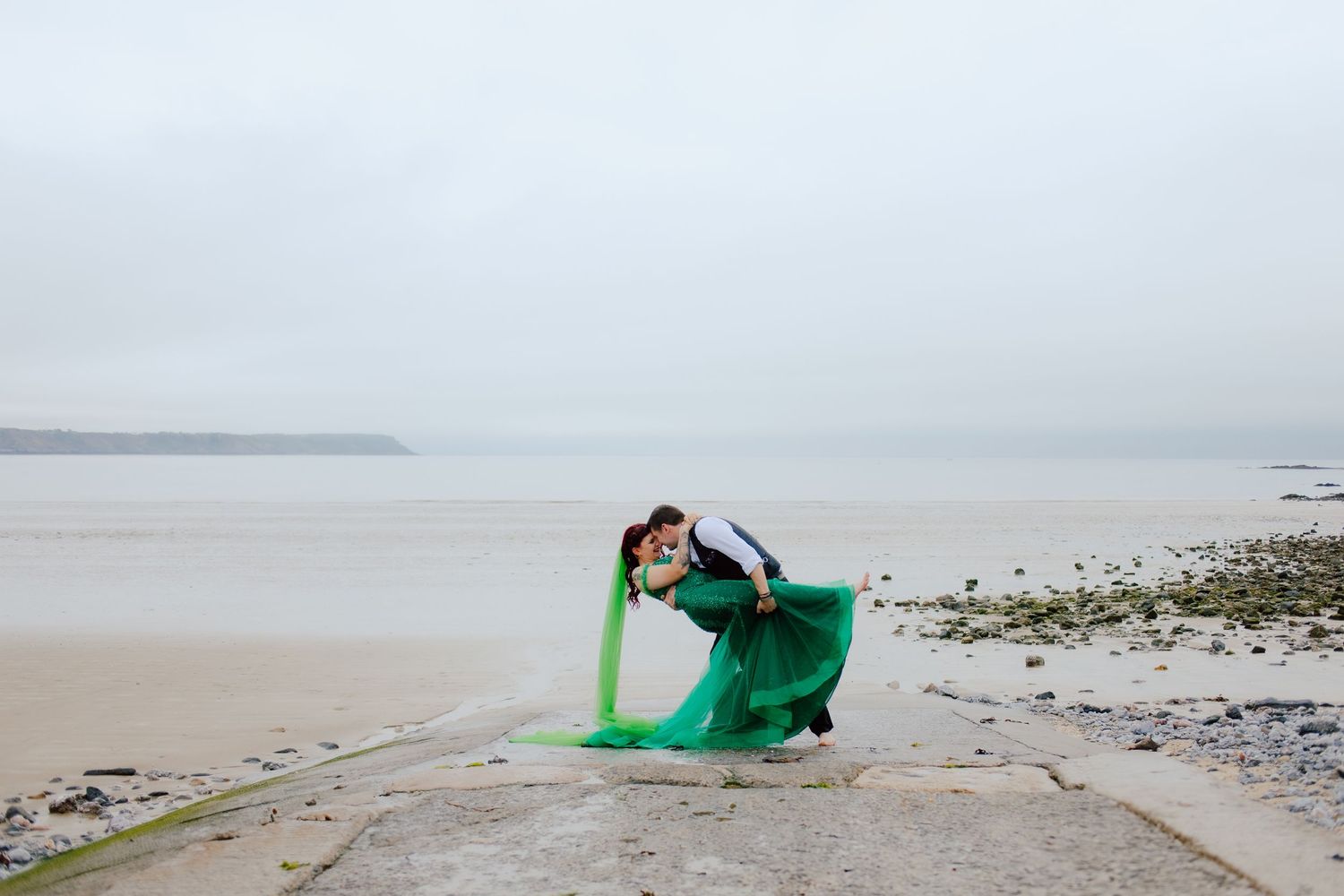Alternative bride wearing a bright green wedding dress on the the beach with her new husband in Swansea.