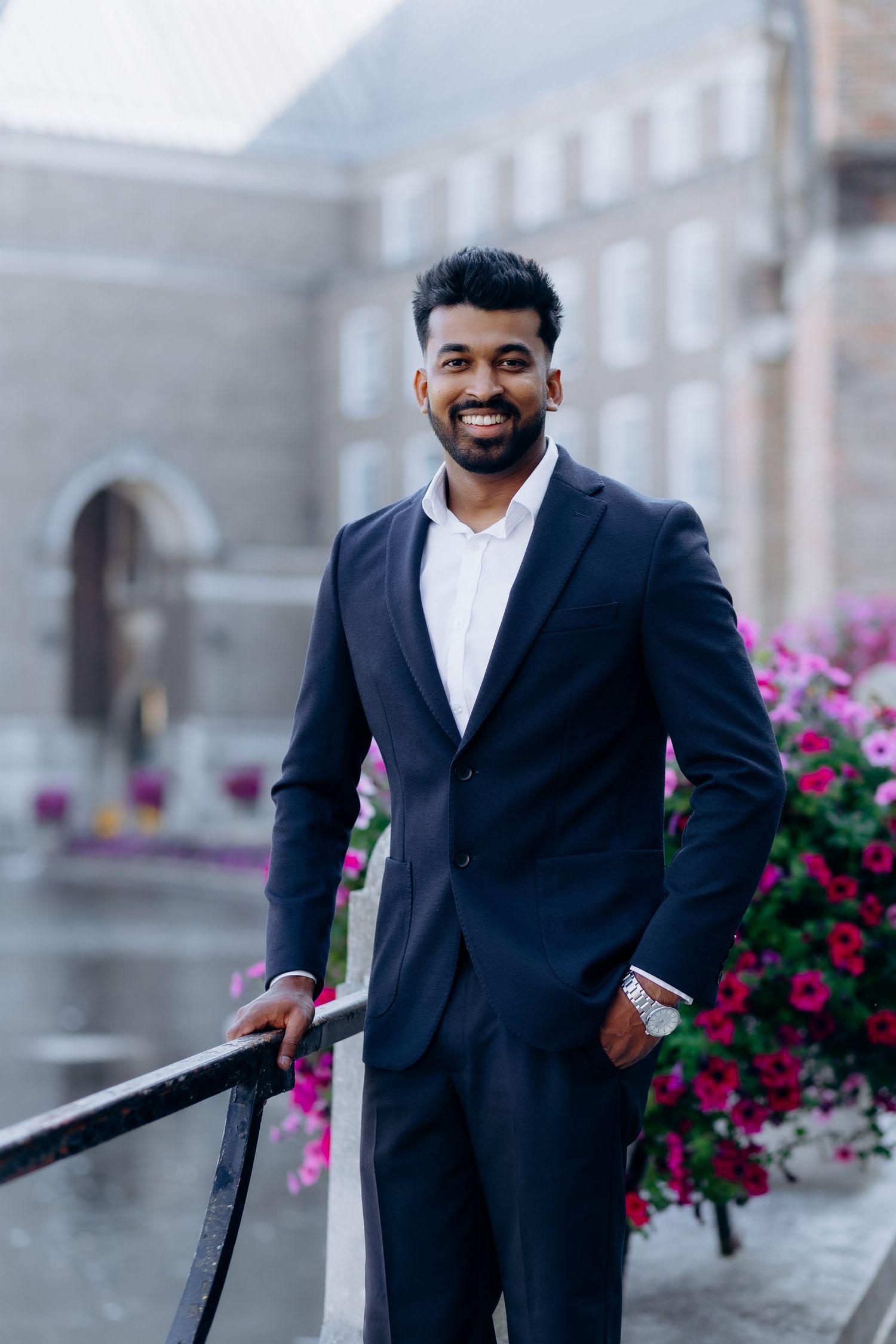 Professional wearing a navy suit and white shirt smiles while posing against a backdrop with pink flowers.