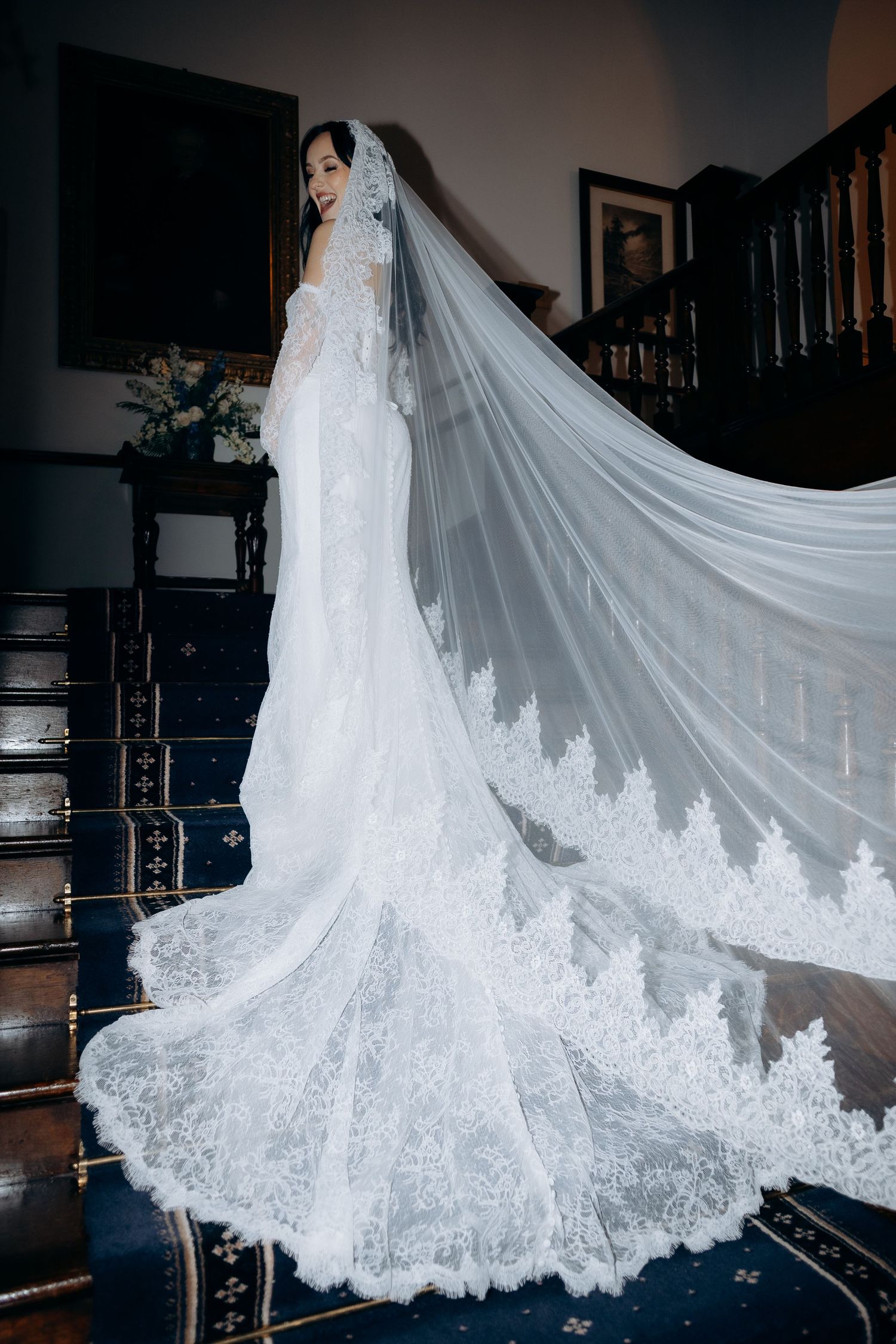 A stunning white lace wedding dress with a dramatic cathedral veil trailing behind in an elegant indoor setting at clearwell castle.