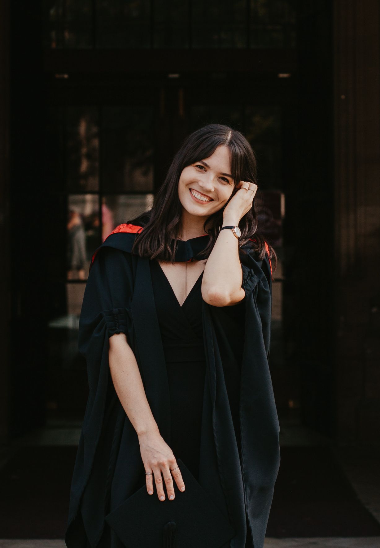 A person in a black dress poses playfully against a dark background.