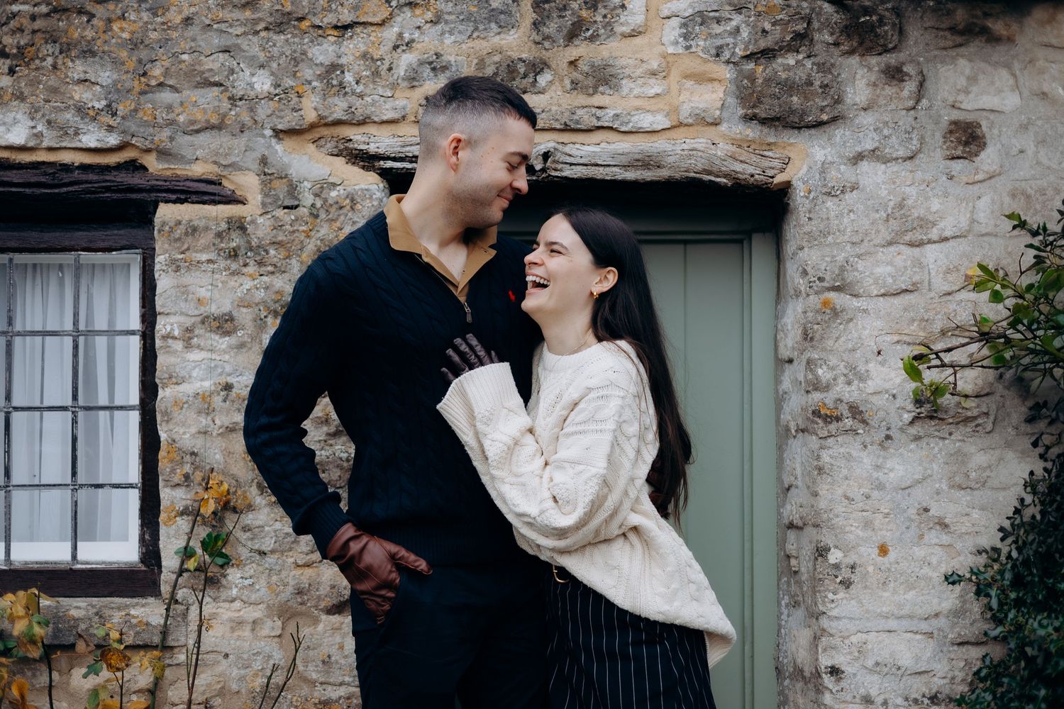 A romantic couple embraces near a rustic stone wall and green door in an intimate outdoor setting.