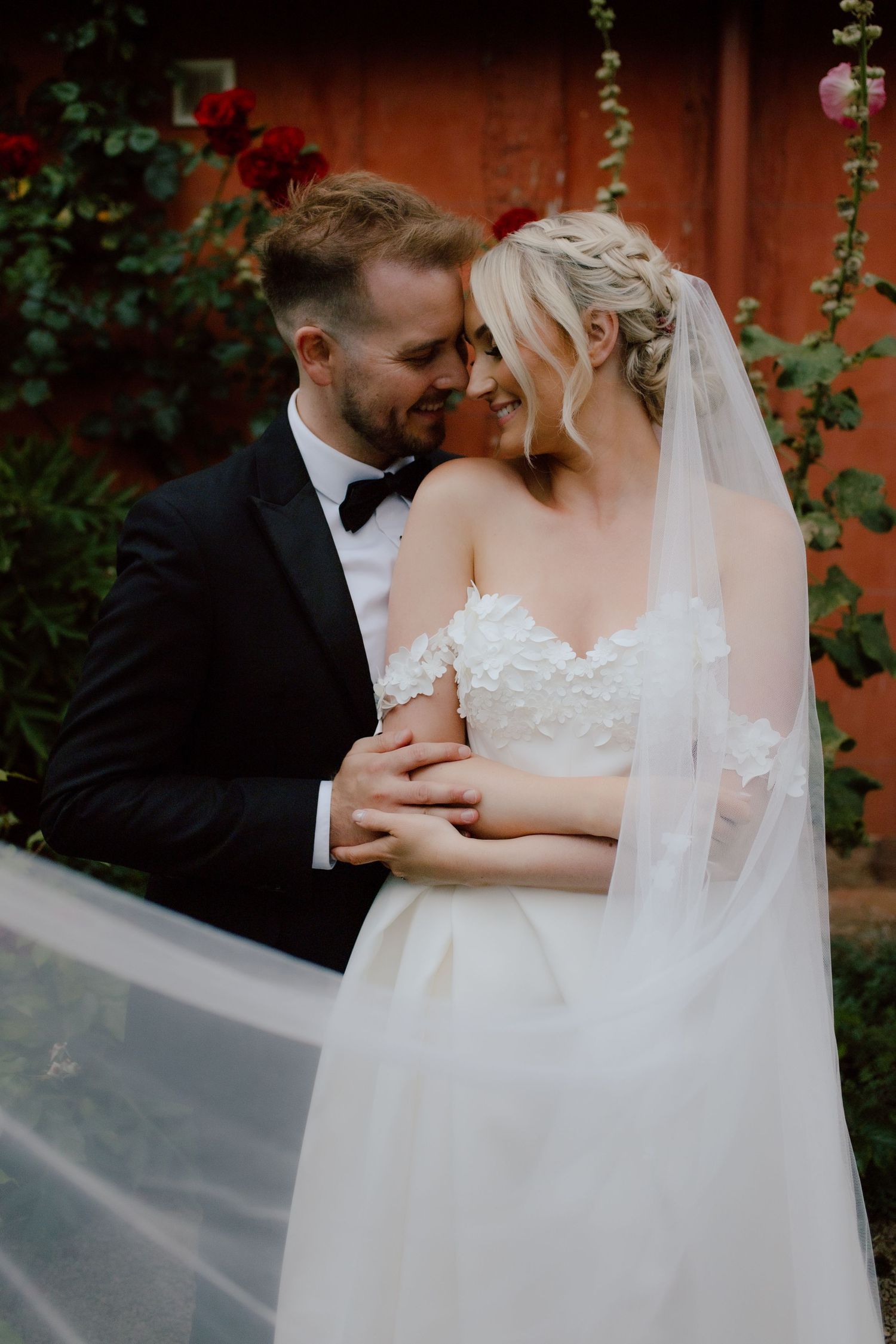A tender moment between newlyweds in a garden setting with a wooden fence and vines in the background at pauntley court.