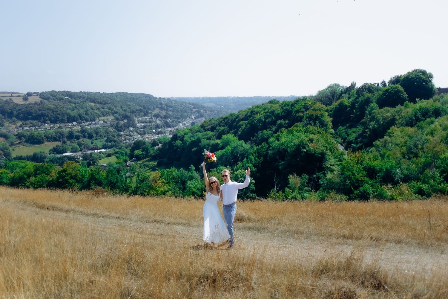 Gloucestershire wedding photoA scenic landscape photo series shows a figure in white moving through golden fields and green hills at sunset.