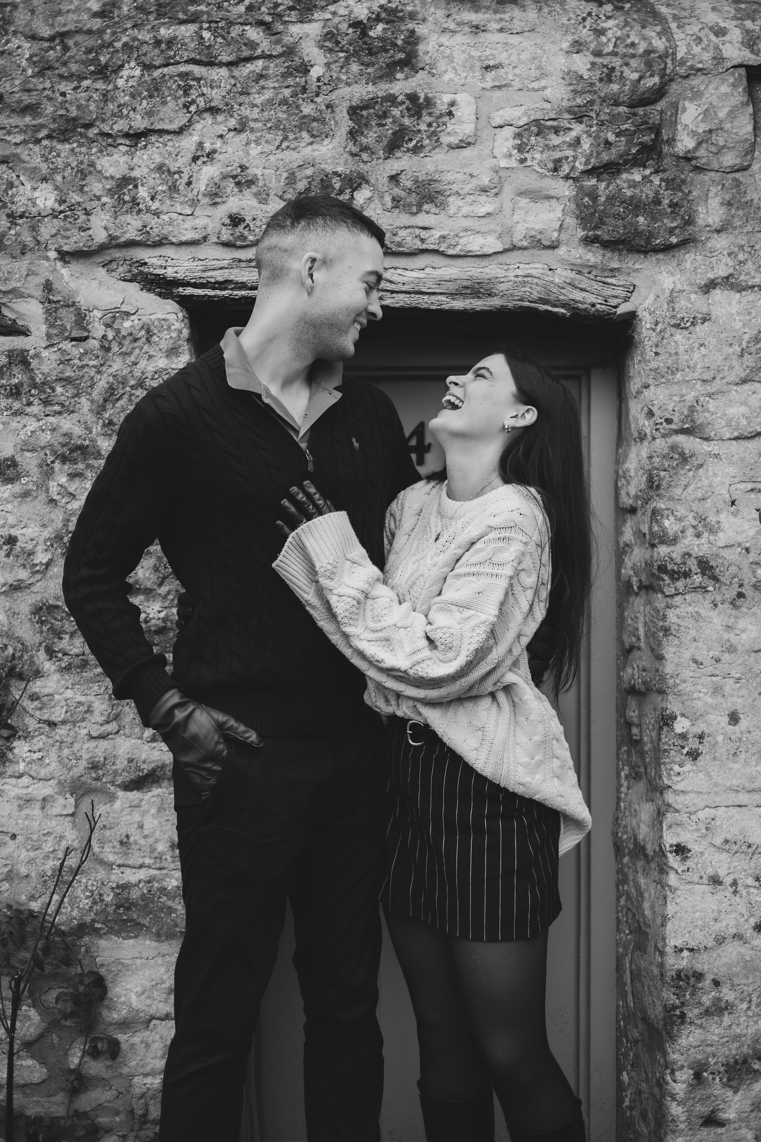 A couple in vintage attire poses dramatically against a rustic stone wall in a series of black and white photos.