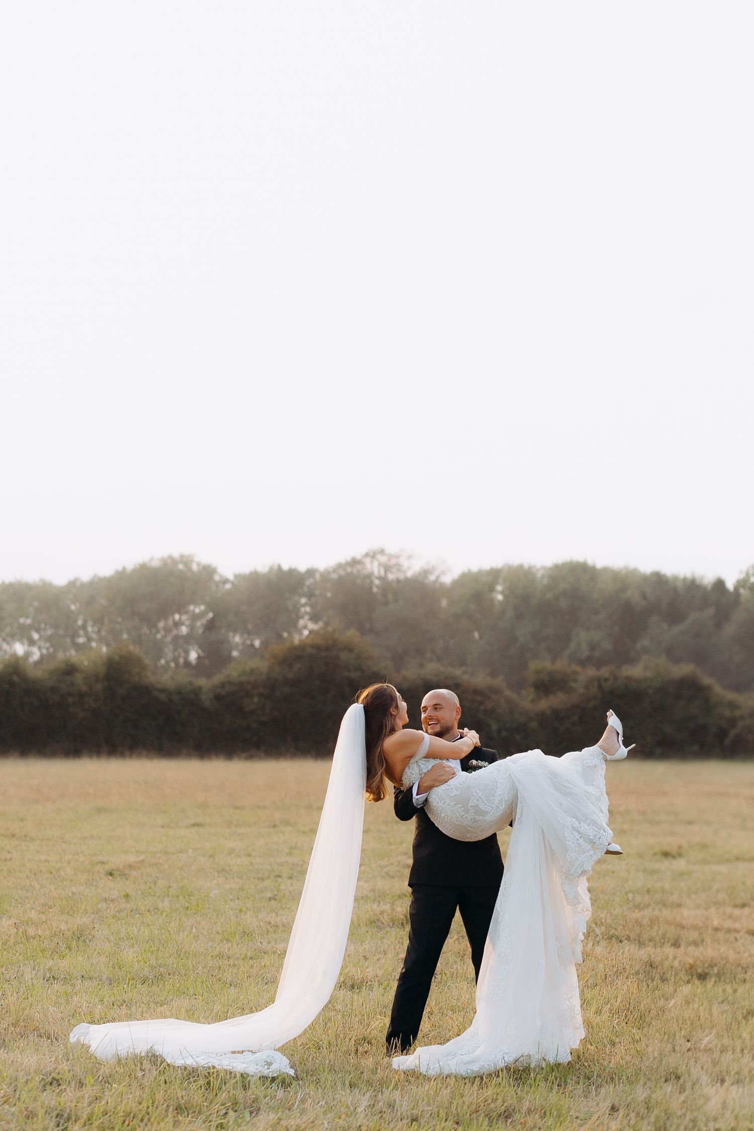 Cotswolds wedding photographer photographs bride and groom walking in a grassy field at sunset.
