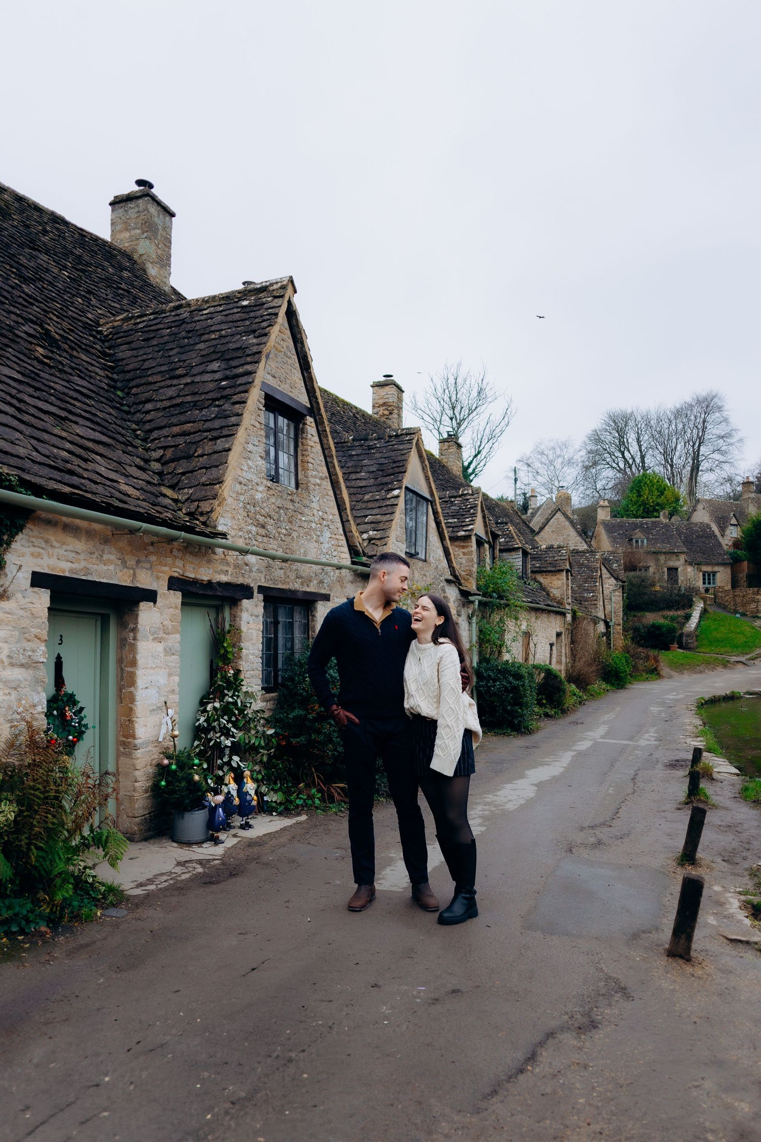 Charming stone cottages line a quaint village street in the English countryside on an overcast day.