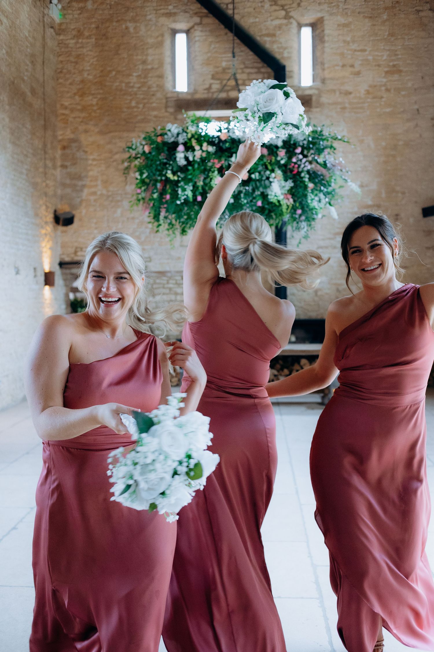 A group of bridesmaids in dusty rose dresses laugh and dance together at Old Gore barn.