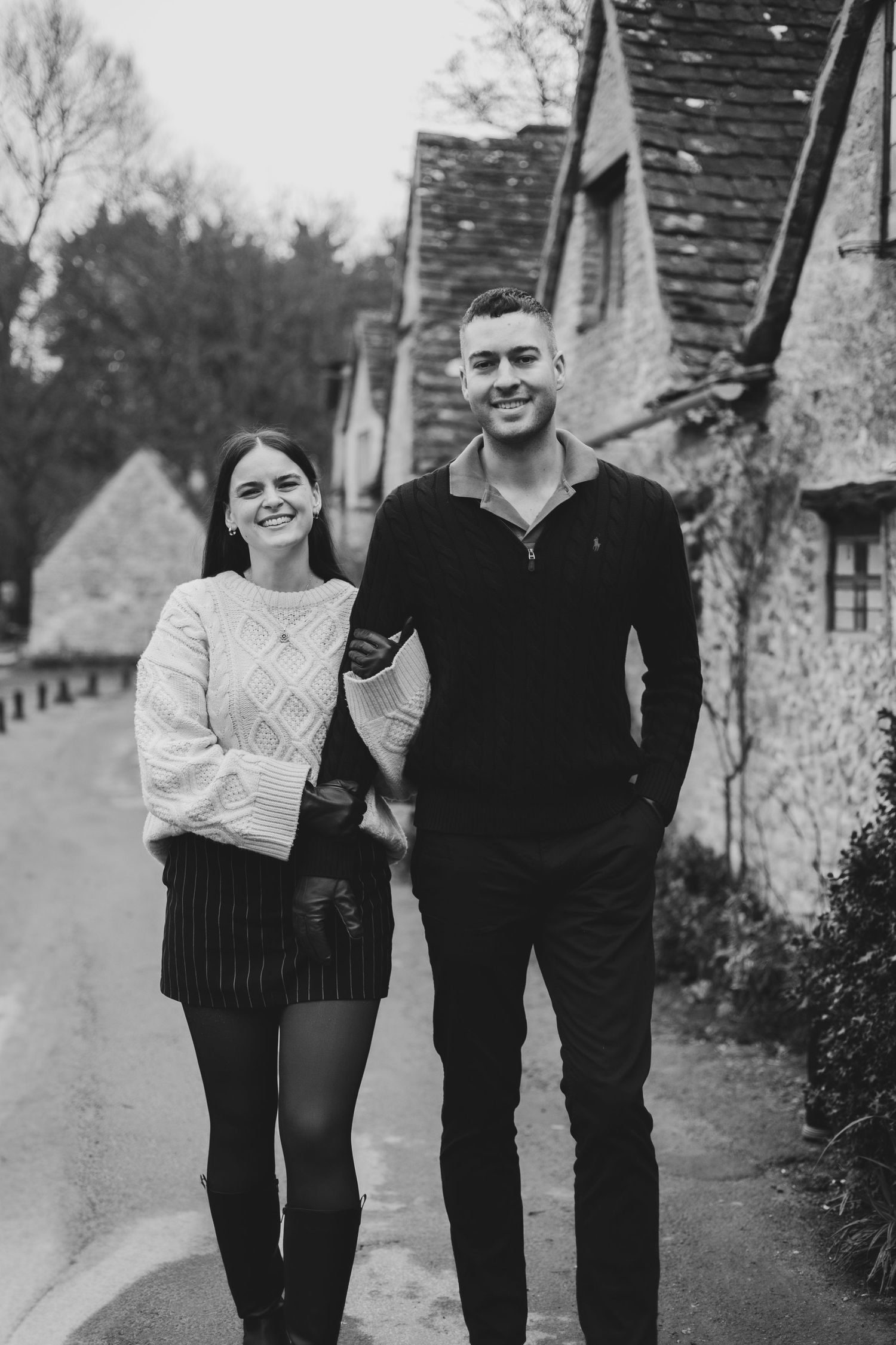 A couple in black and white clothing walking together on a path in winter with bare trees in the background.