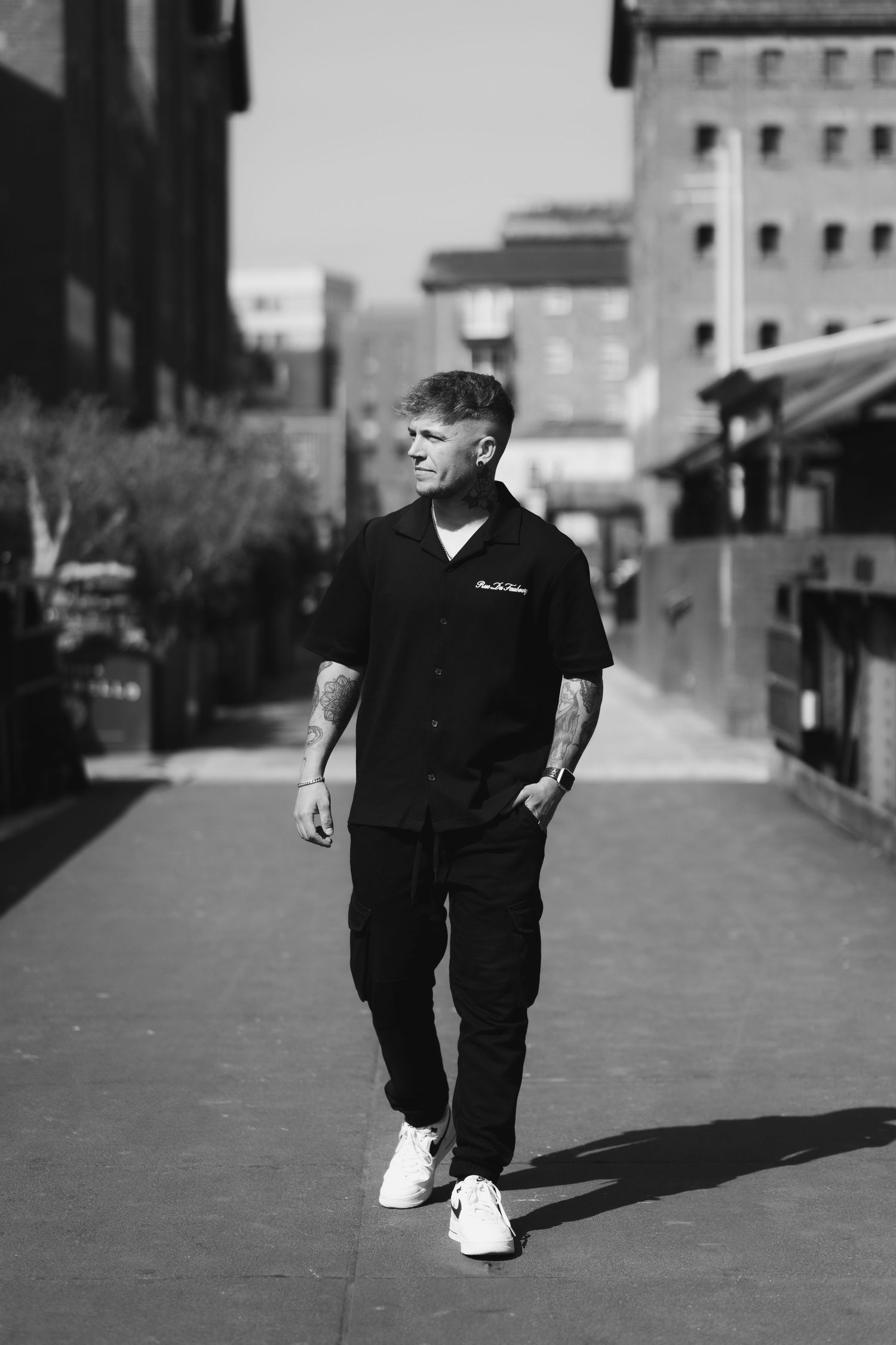 Black and white photograph of a person walking on a city street casting a long shadow in dramatic lighting.