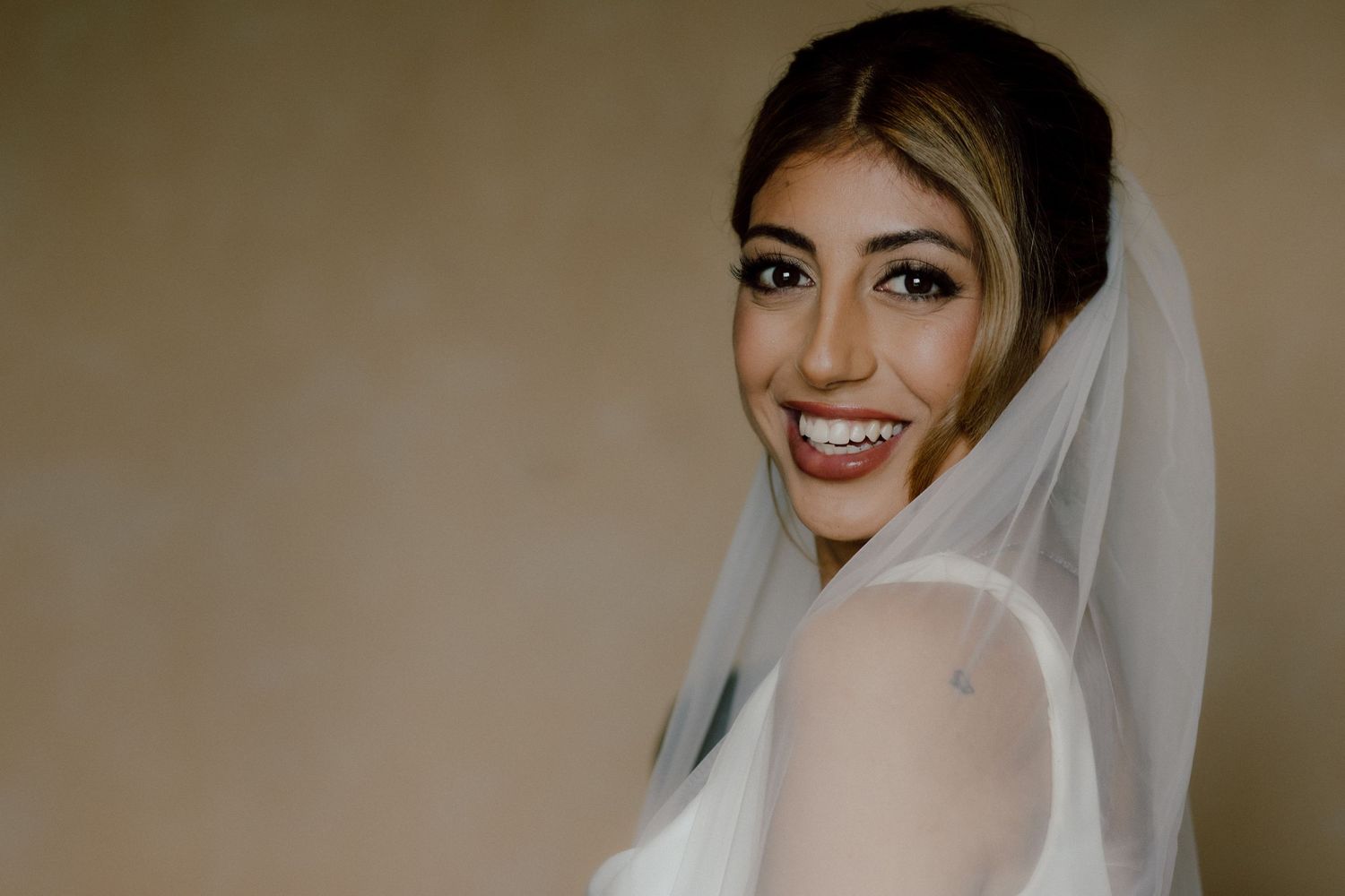 Portrait of a radiant bride wearing a delicate veil against a neutral backdrop.