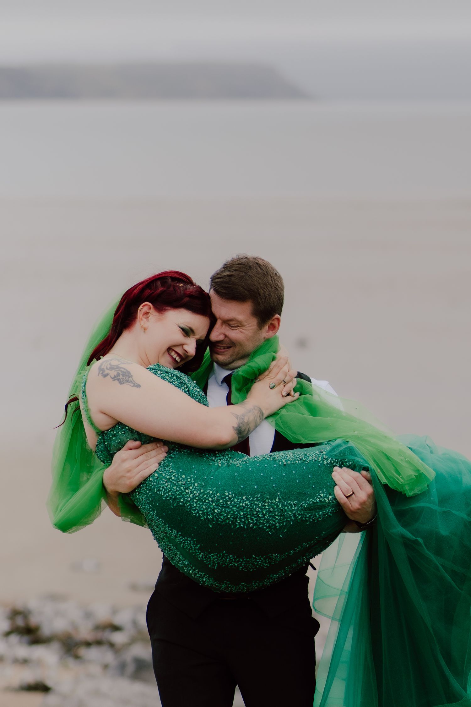 A romantic couple in formal wear embrace and dance, with the woman wearing a flowing emerald green gown against a cloudy sky.