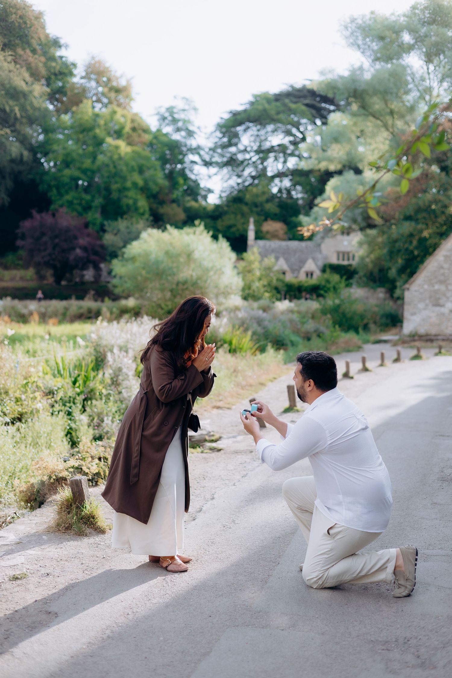 Man in white kneels to propose to woman in Arlington row Bibury captured by a cotswolds proposal photographer.