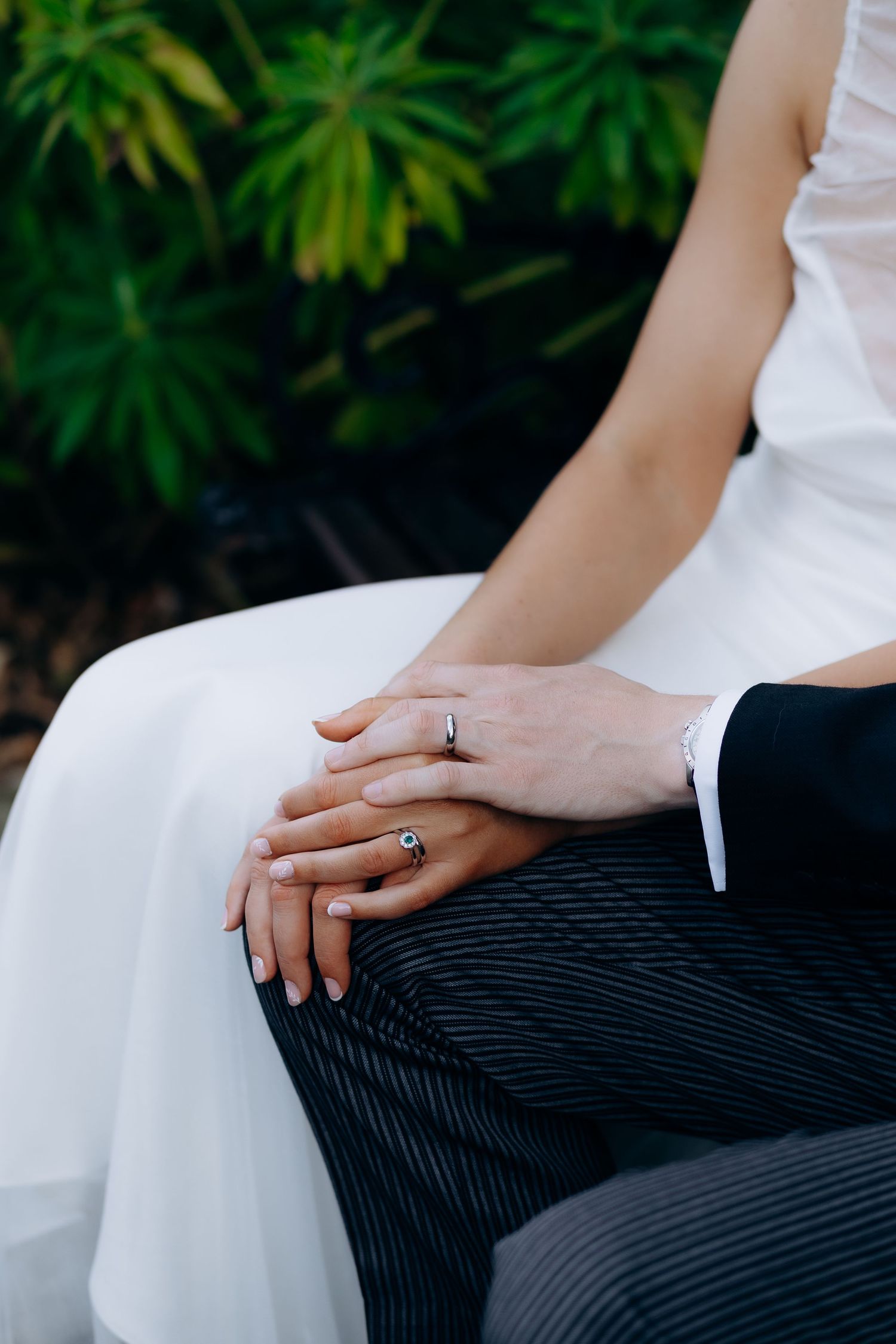 A close-up series of hands showing a wedding ring against formal black and white attire with green foliage in background.
