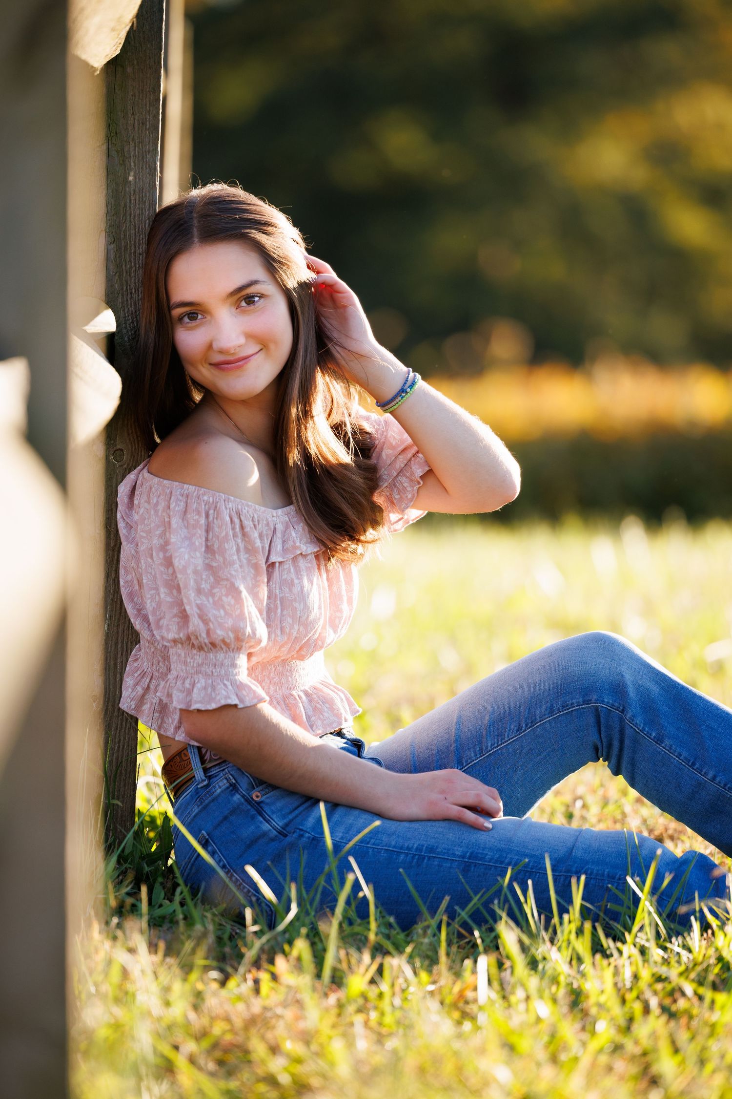Portrait in a field at golden hour showing someone sitting in grass wearing an off-shoulder top and blue jeans.